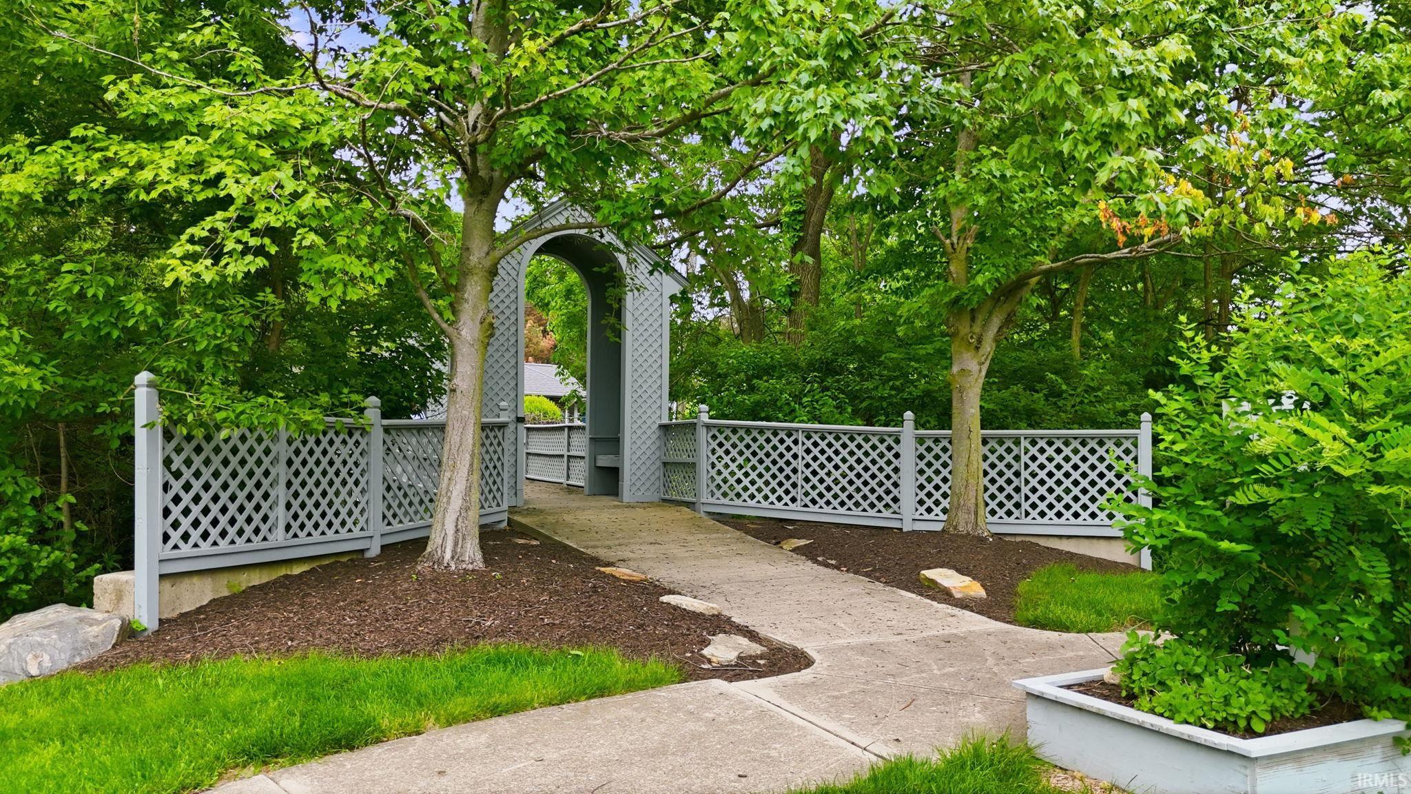 Arched lattice gateway with a concrete pathway and lush landscaping