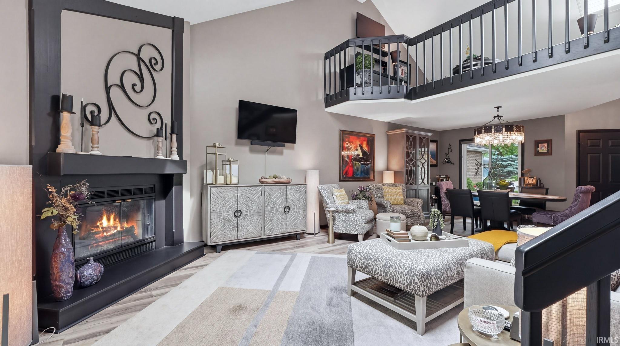 Two-story living area featuring a prominent fireplace with a dark mantel, wood-finish flooring, and a second-story interior balcony with dark railings