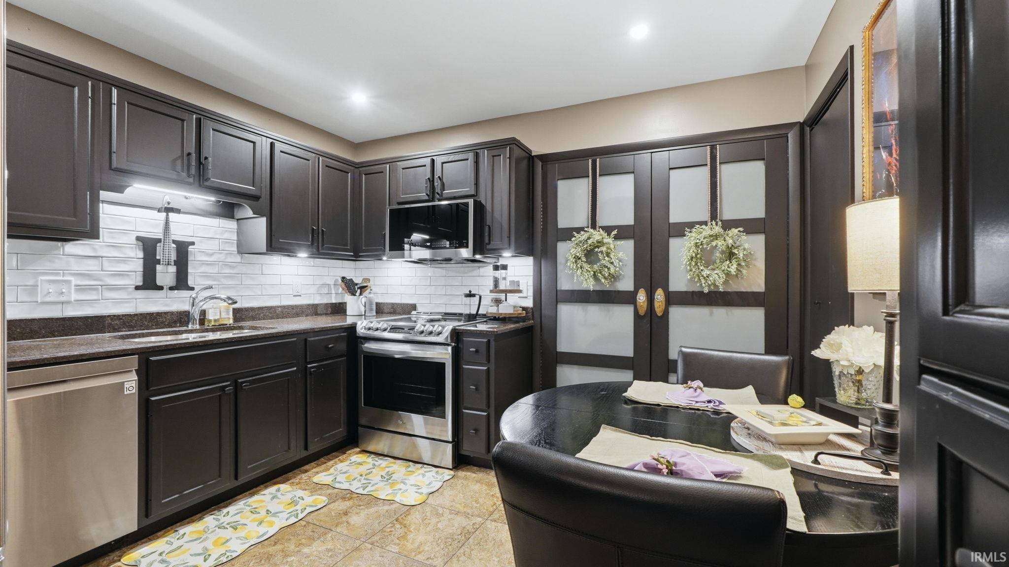 Kitchen featuring dark cabinetry, stainless steel appliances, a white subway tile backsplash, and recessed lighting