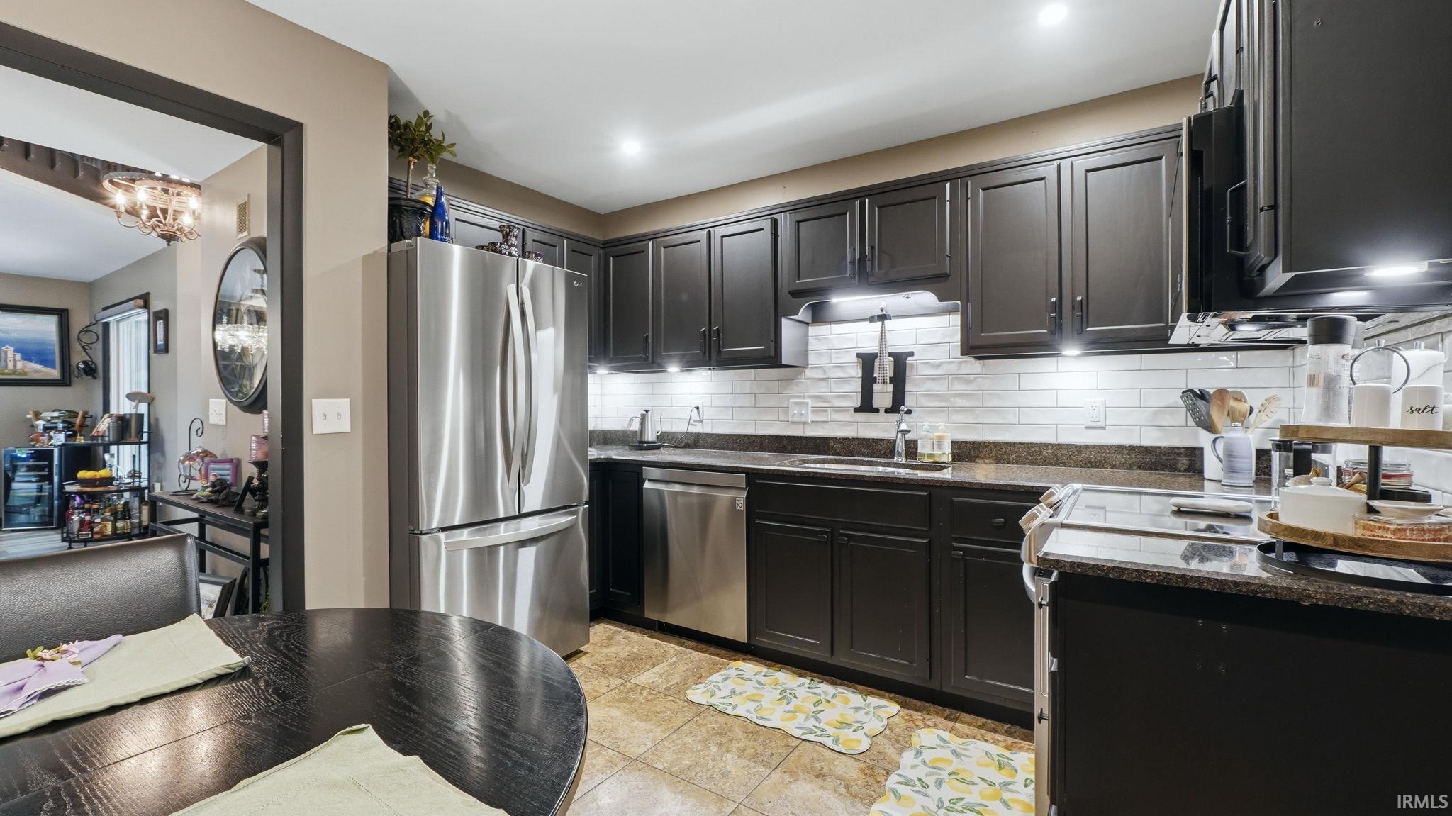 Kitchen featuring dark cabinetry with brushed nickel hardware, stainless steel appliances, a subway tile backsplash, and dark countertops
