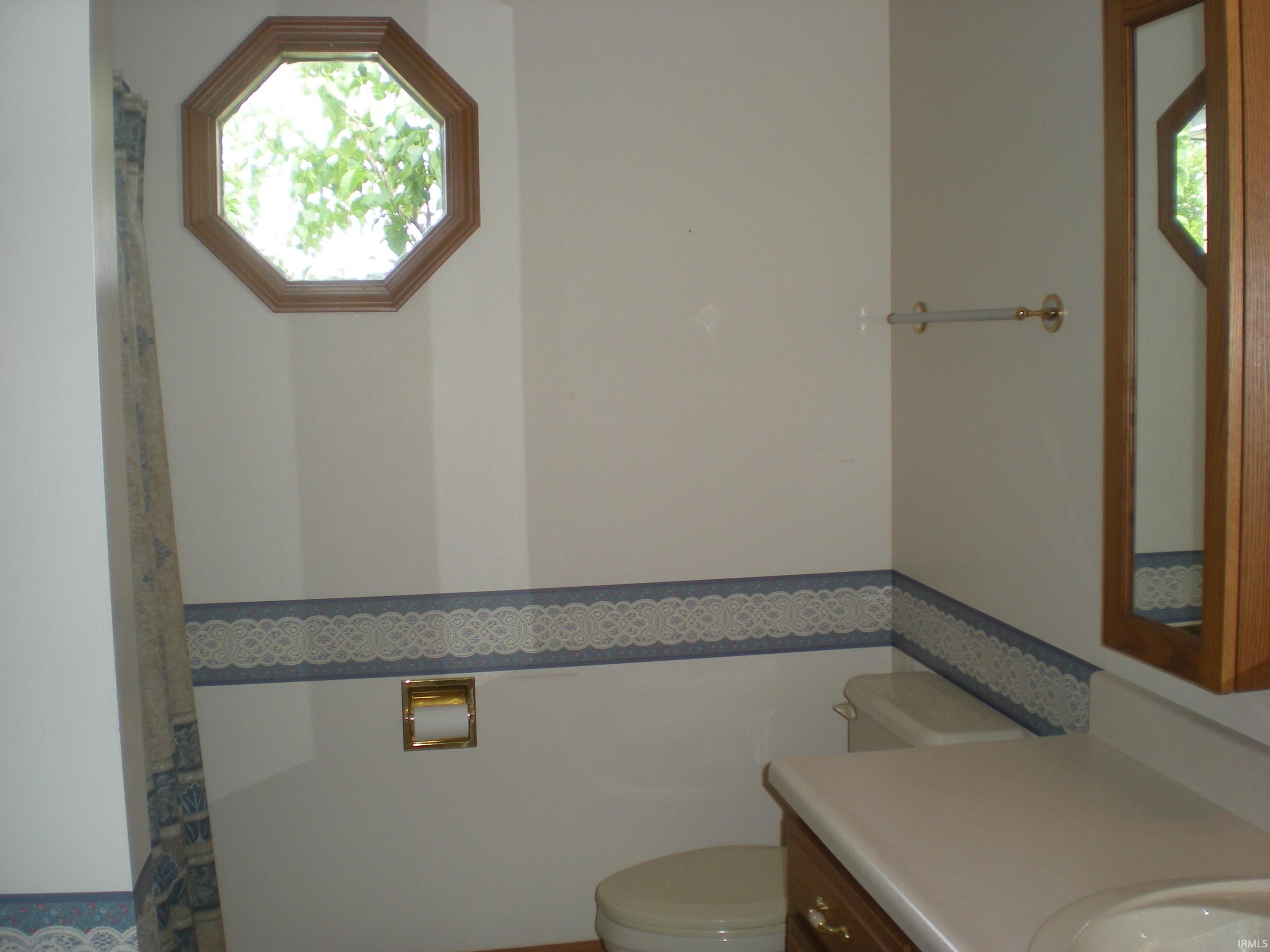 Bathroom featuring an octagonal window with wood trim, a built-in vanity with a laminate countertop, and a toilet