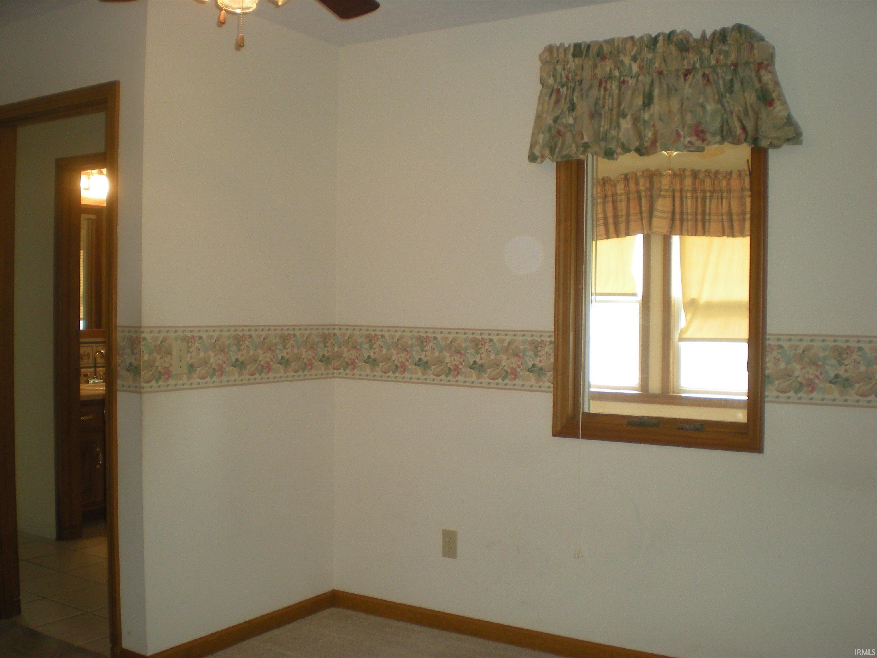 Bright interior space featuring a double-hung window with wood trim, ceiling fan, and a neutral wall finish