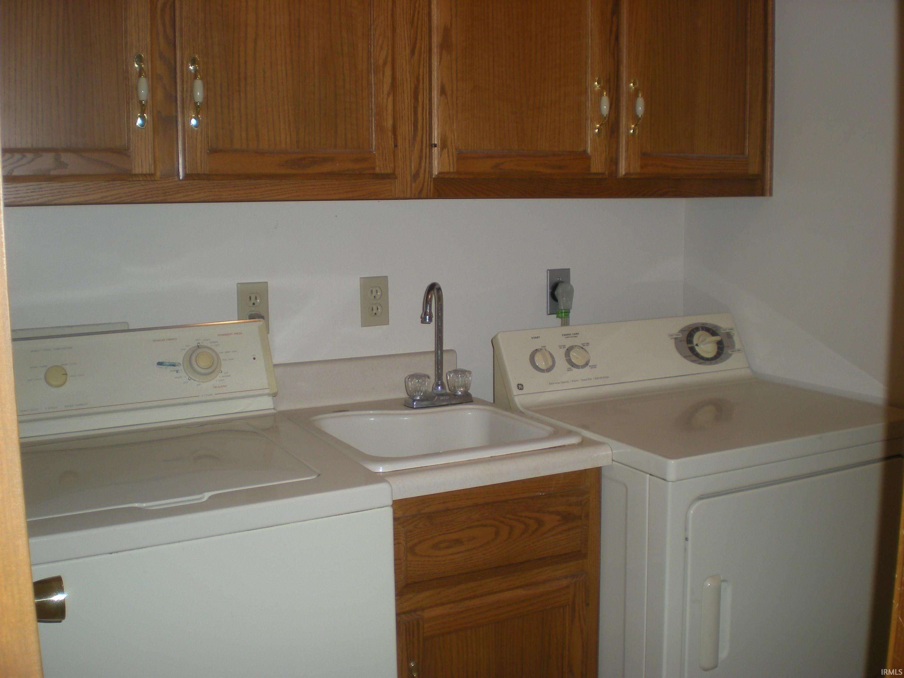 Dedicated laundry area featuring wood cabinetry, a utility sink with a chrome faucet, and white countertop space