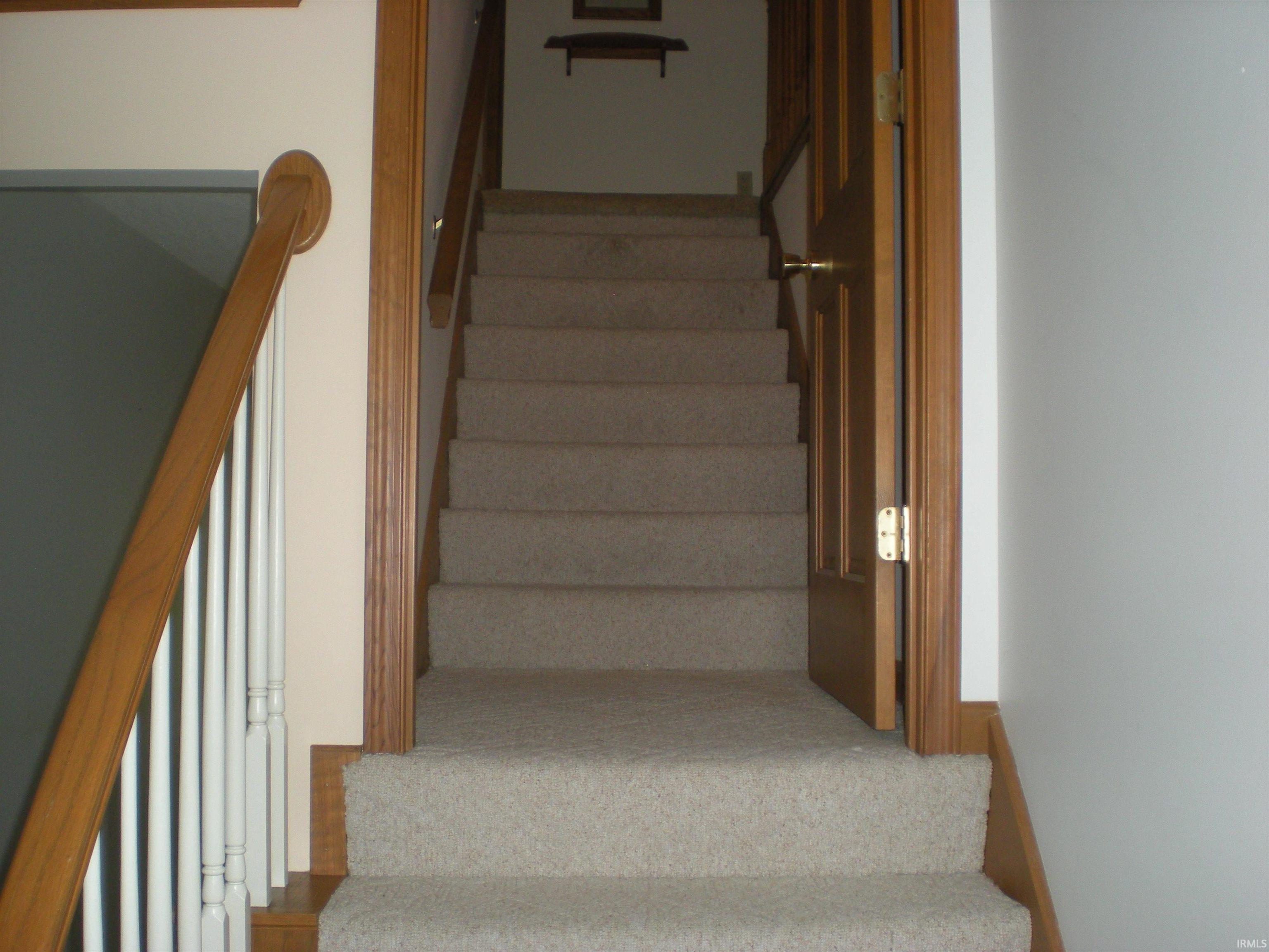 Staircase featuring carpeted treads, wood-finish handrail, and white balusters