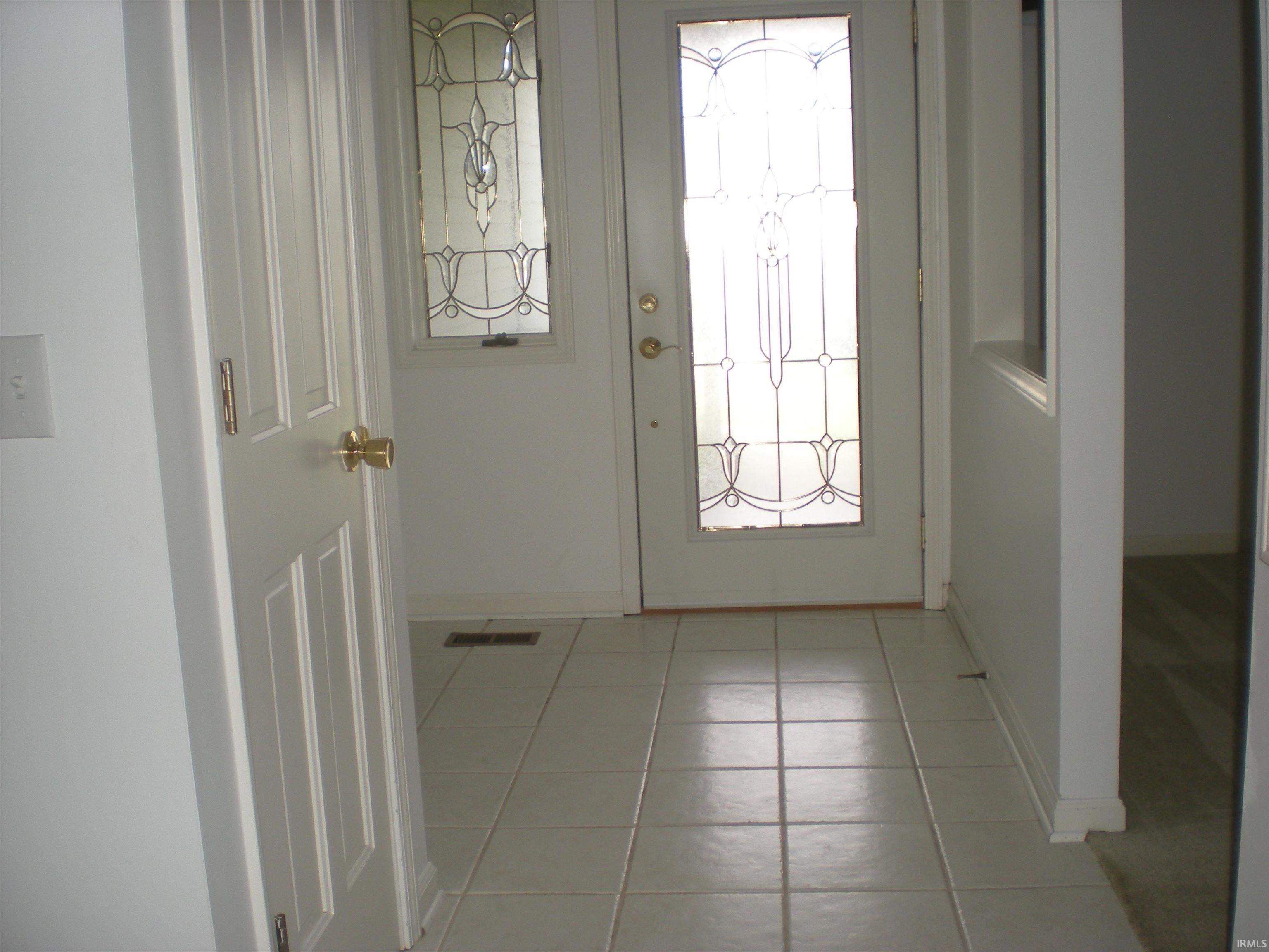 Entryway featuring a decorative glass panel door and sidelight, ceramic tile flooring, and a six-panel interior door with brass hardware