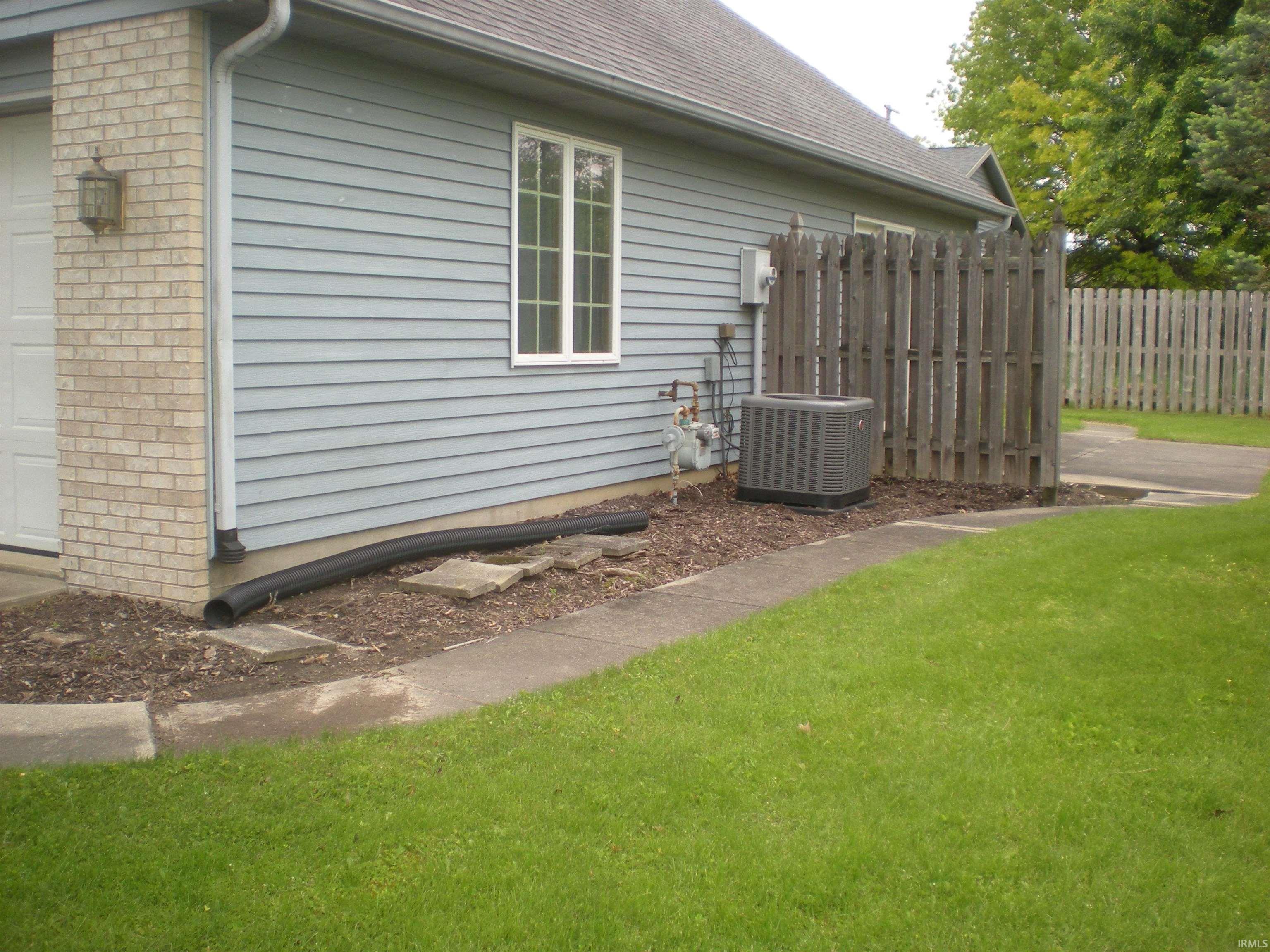 Exterior featuring light blue siding, a brick facade, a white-framed window, and a wooden privacy fence