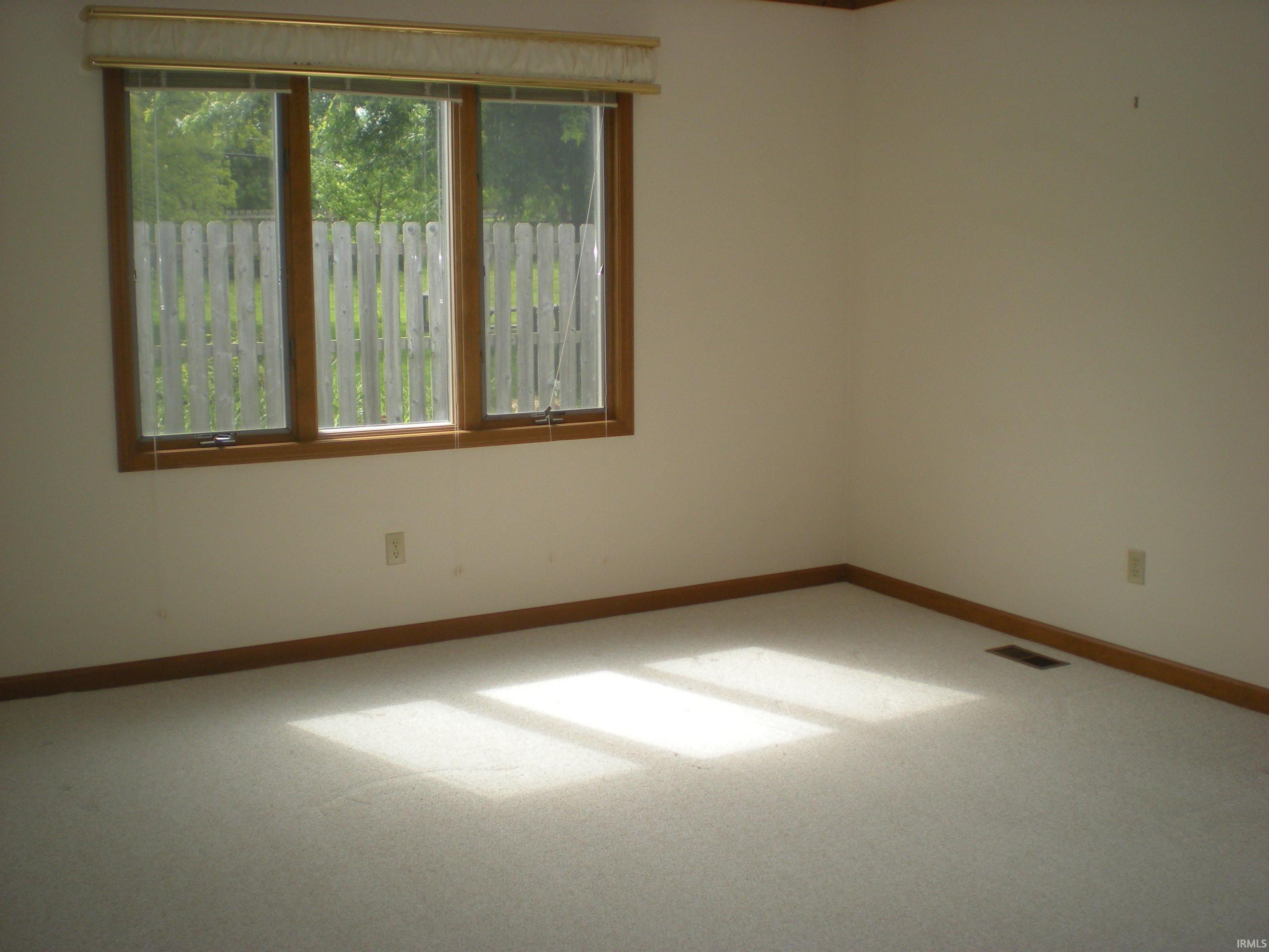 Triple window unit with wood trim, neutral carpeting, and light-toned walls