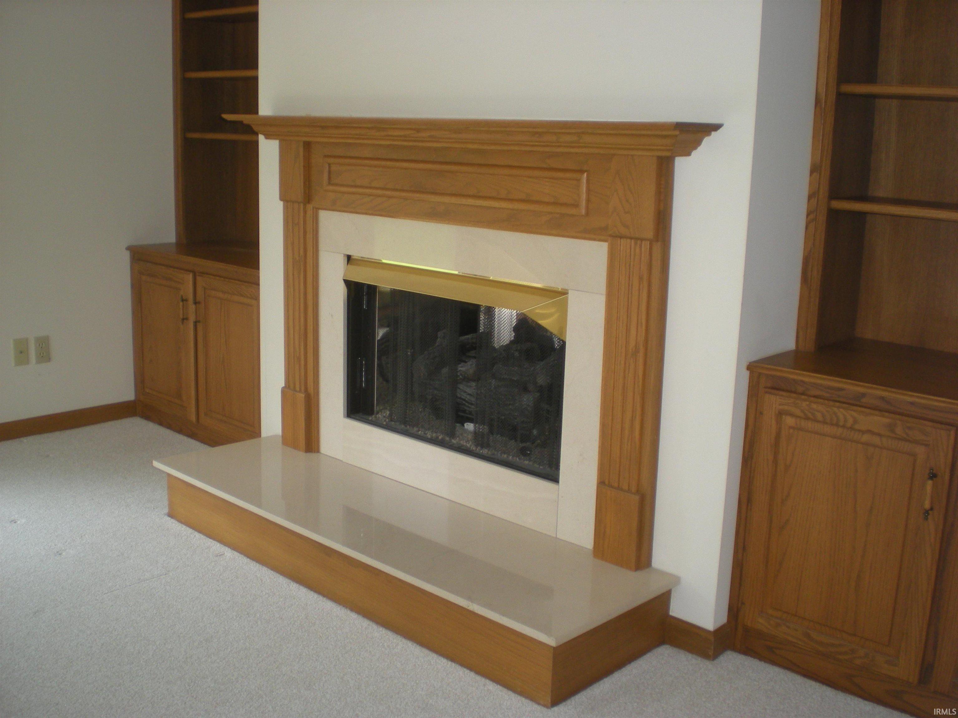 Fireplace featuring a wood mantel, light-toned surround, and hearth, flanked by built-in wood cabinetry with shelving