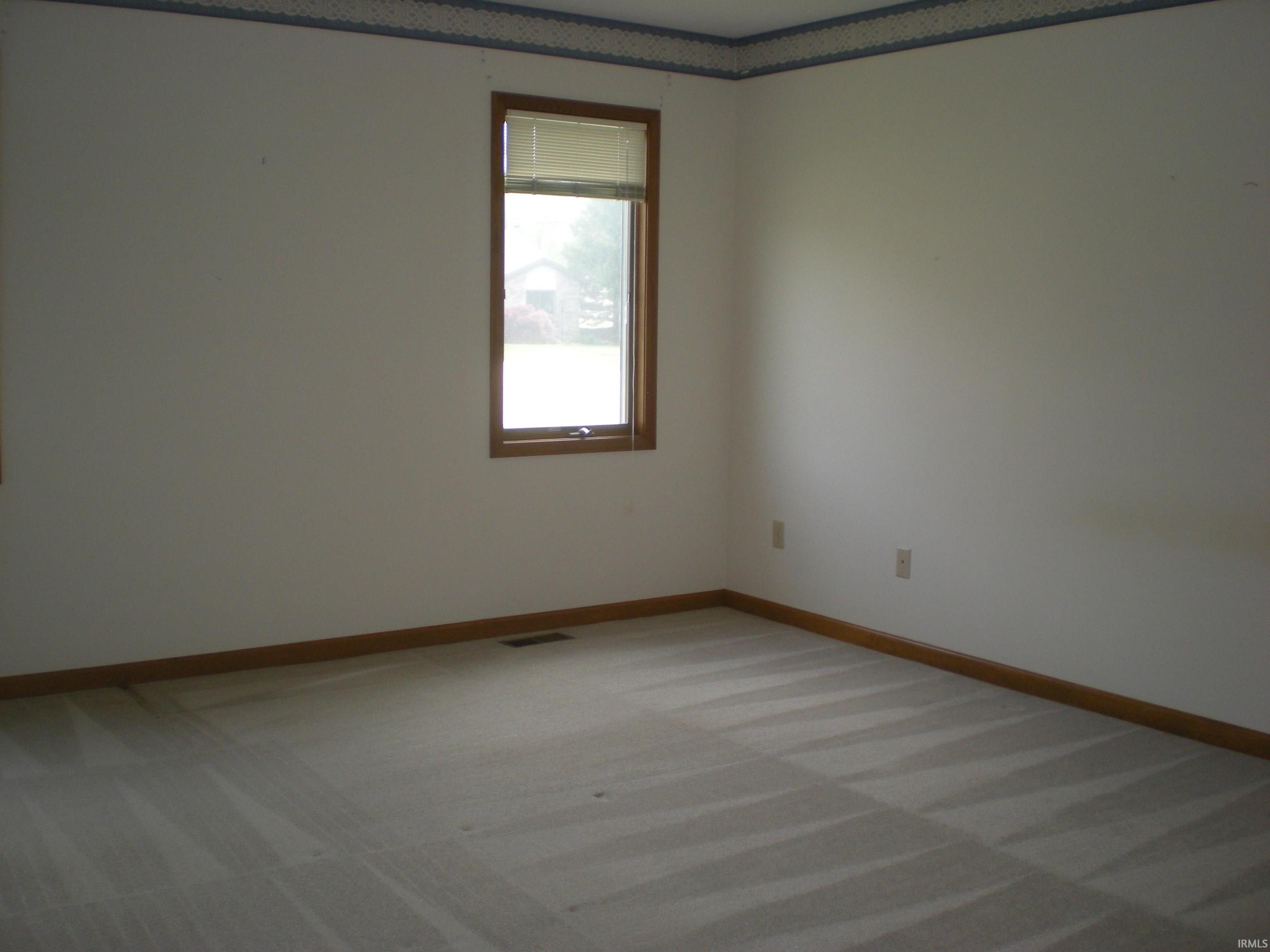 Neutral-toned carpeting paired with white walls, wood window trim, and wood baseboards