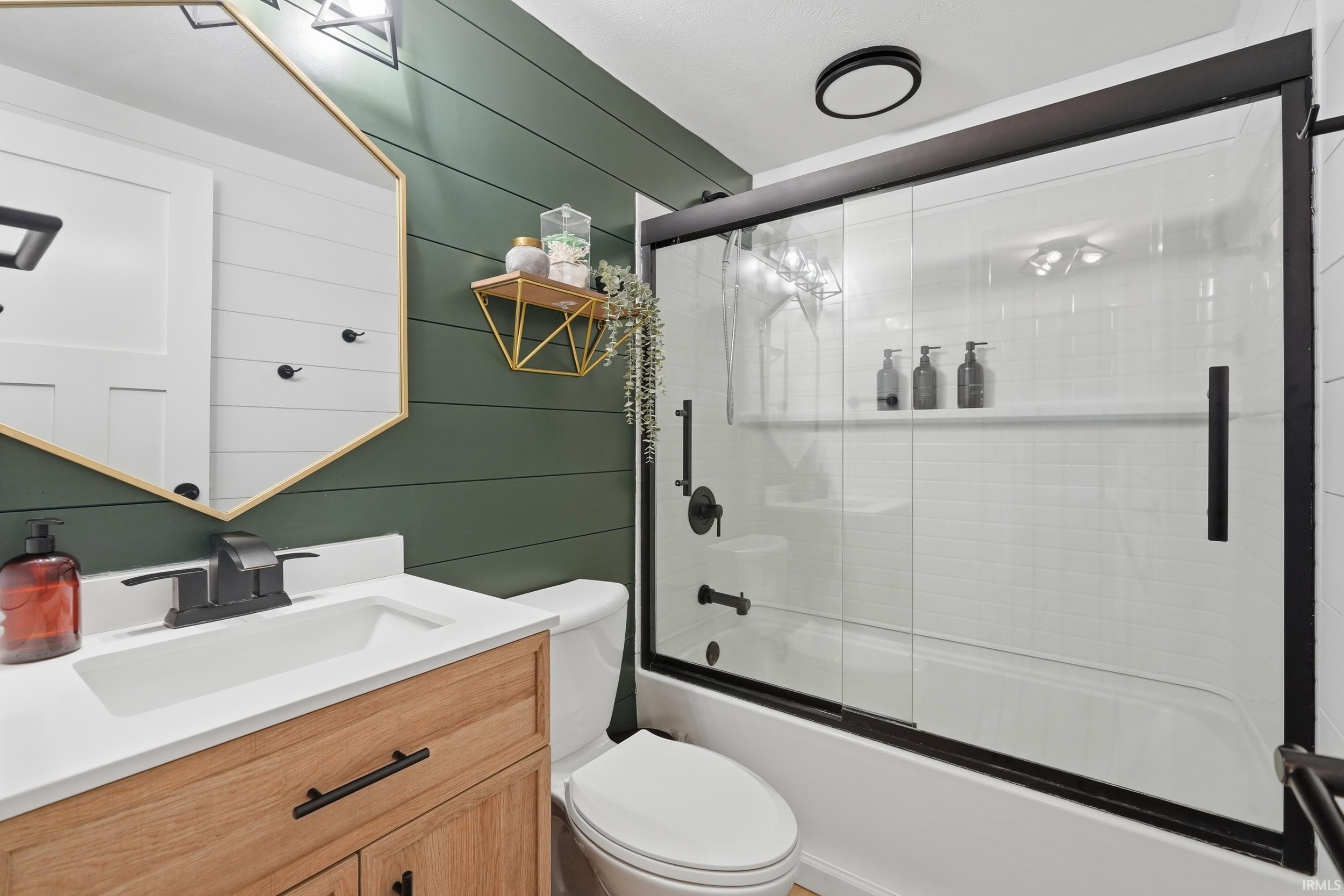 Bathroom featuring a wood-finish vanity with a white countertop and integrated sink, matte black faucet hardware, and a gold-framed hexagonal mirror