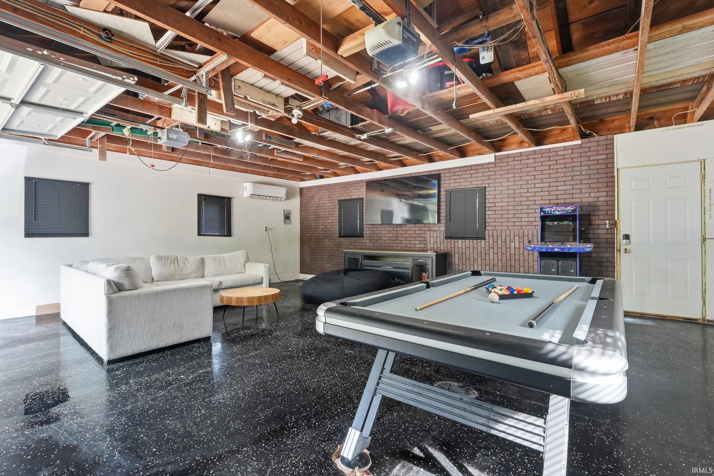 Entertainment area featuring a textured brick accent wall, durable epoxy flooring, and exposed timber ceiling joists
