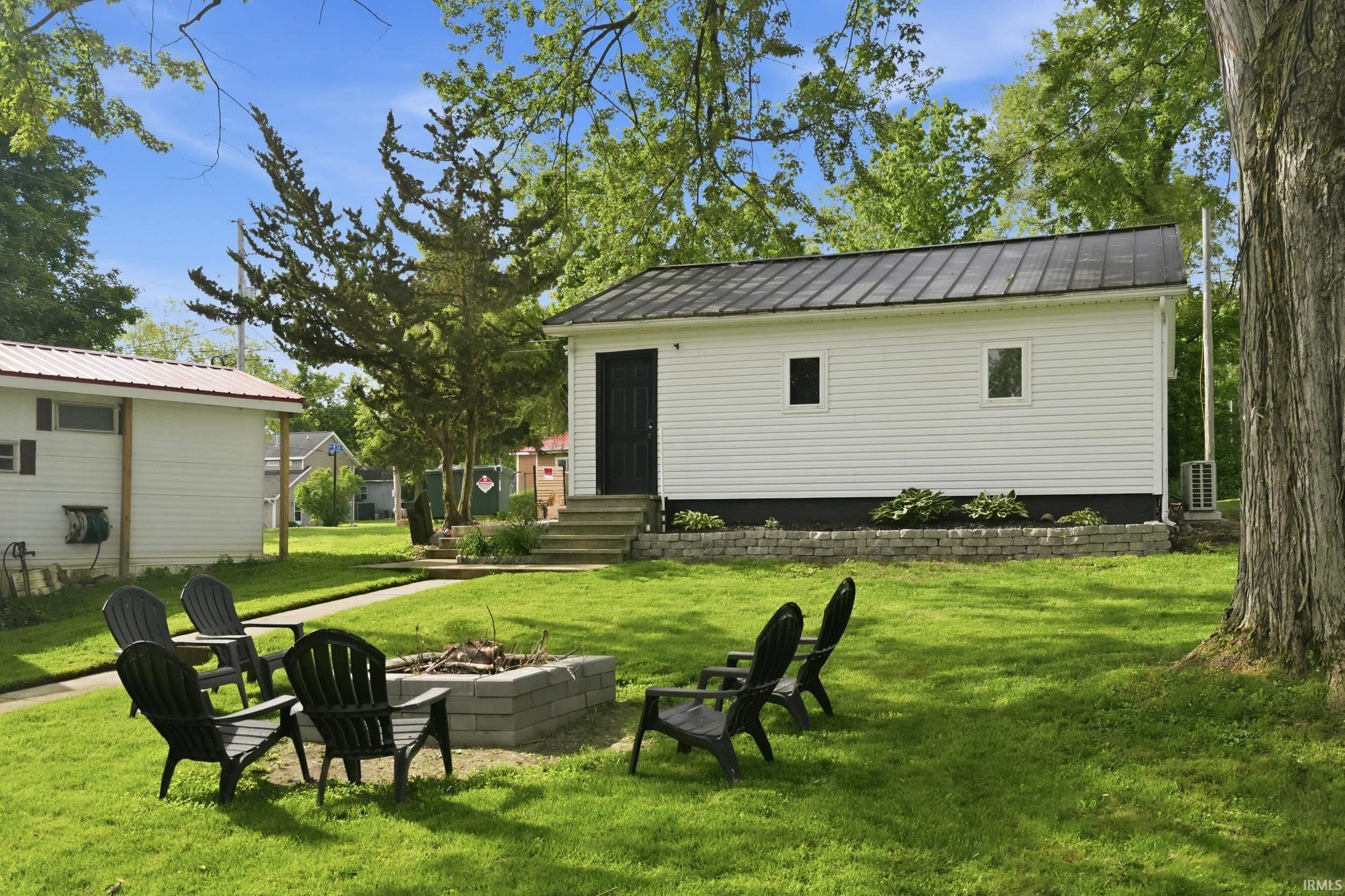 Manicured lawn featuring a stone fire pit, surrounded by mature trees
