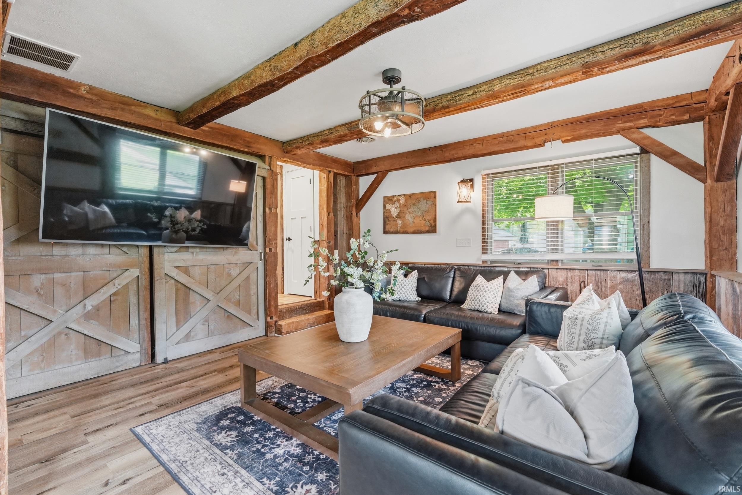 Living area featuring exposed wood beams, wood-finish flooring, and a large window with blinds