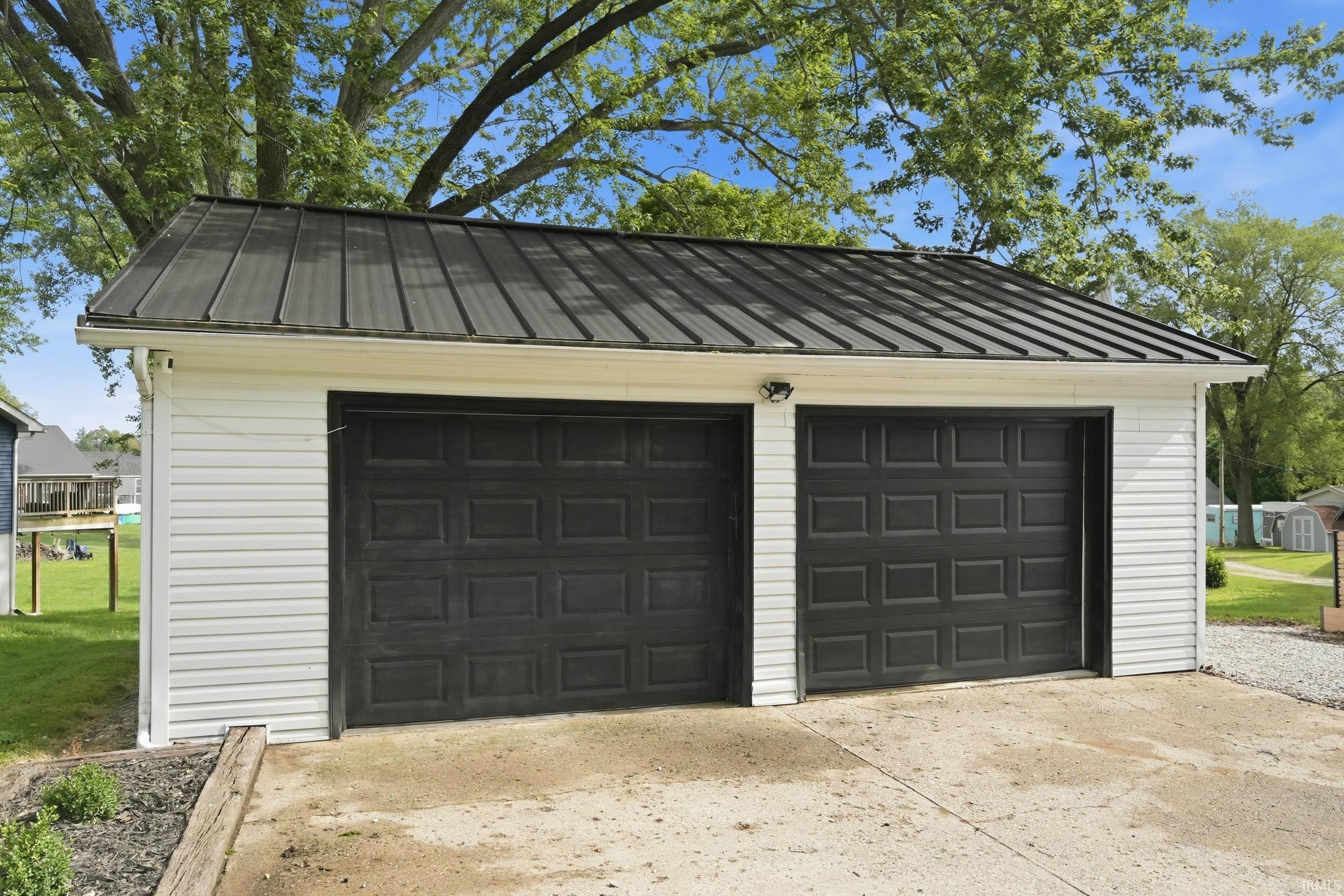 Two-car garage featuring white siding, a dark metal roof, and concrete paving