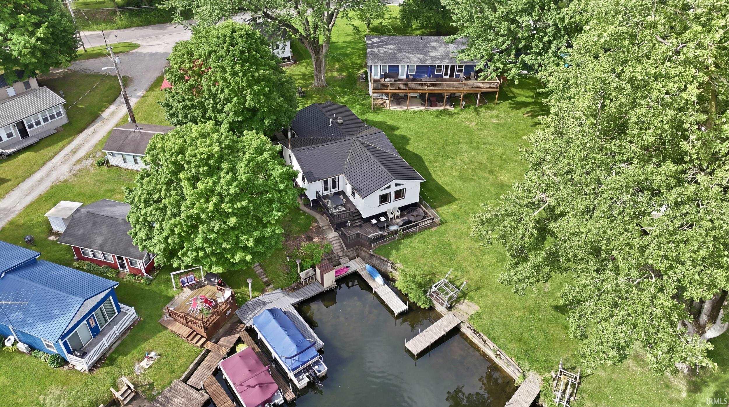 Waterfront property featuring multiple docks, direct water access, a spacious lawn, and mature trees