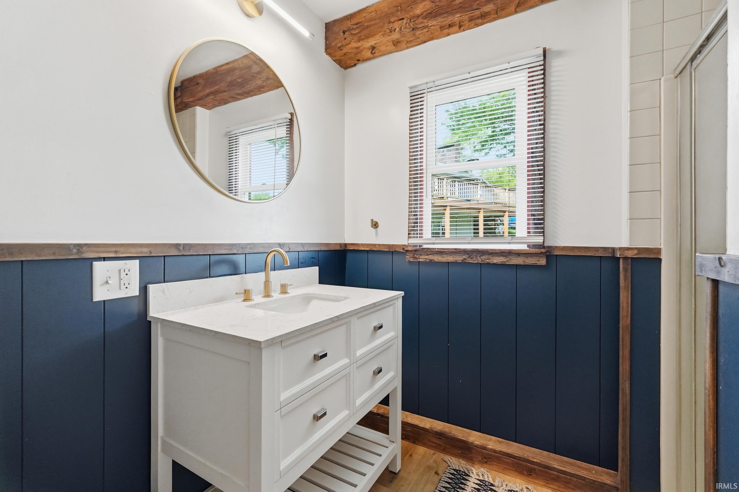Bathroom featuring a white vanity with a white countertop and gold-tone faucet, blue wainscoting, and wood-finish flooring