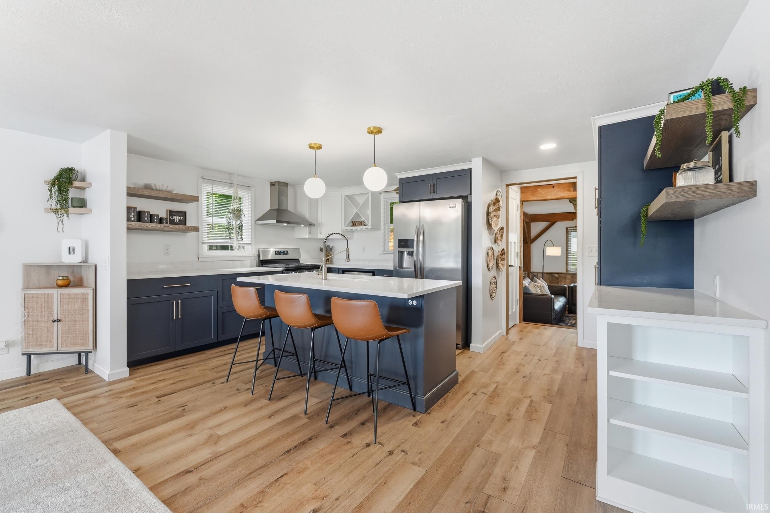 Modern kitchen featuring wood-finish flooring, two-tone cabinetry, a central island with seating, a stainless steel appliance suite, and open shelving