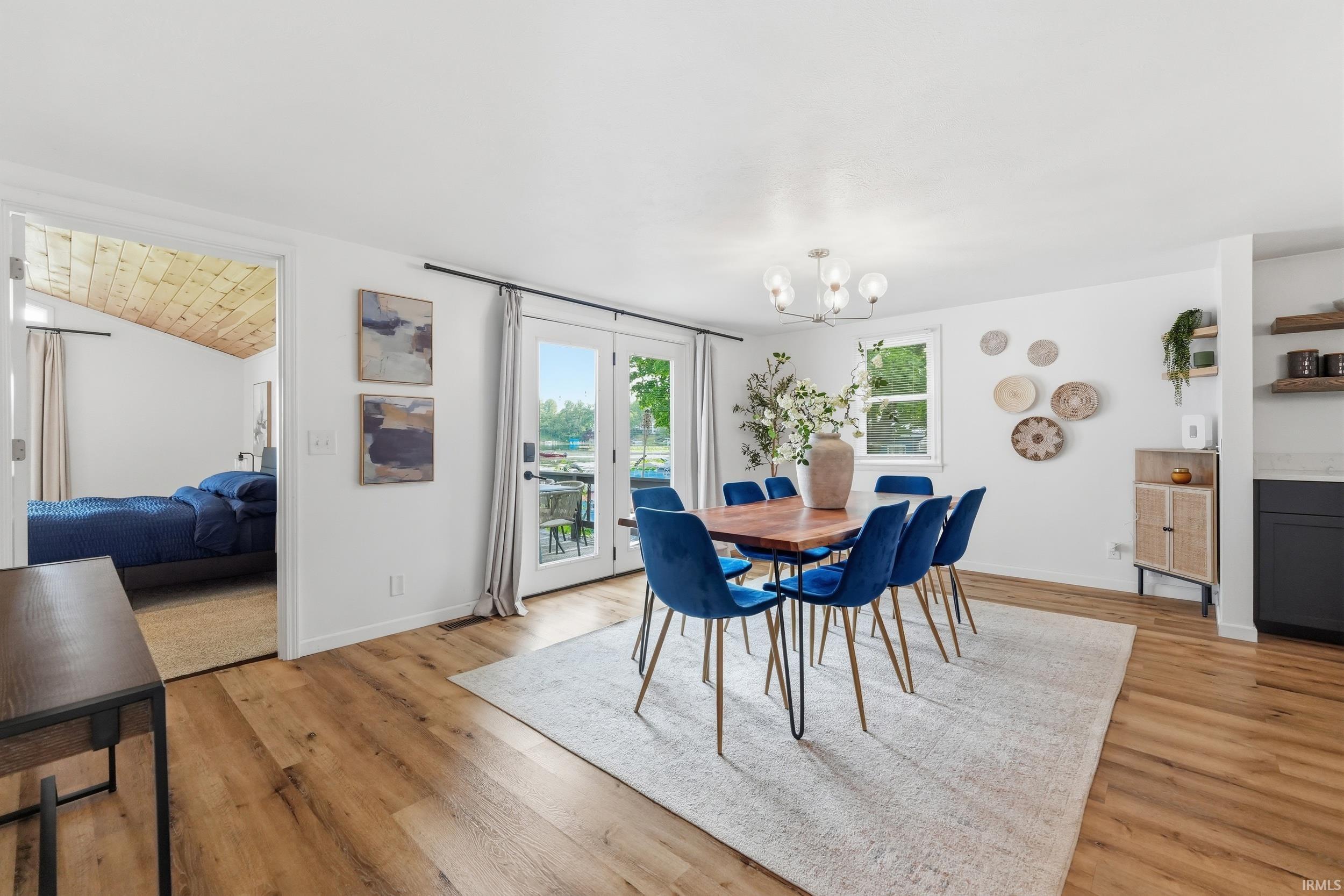Open-concept dining area featuring wood-finish flooring, a contemporary chandelier, and double glass doors