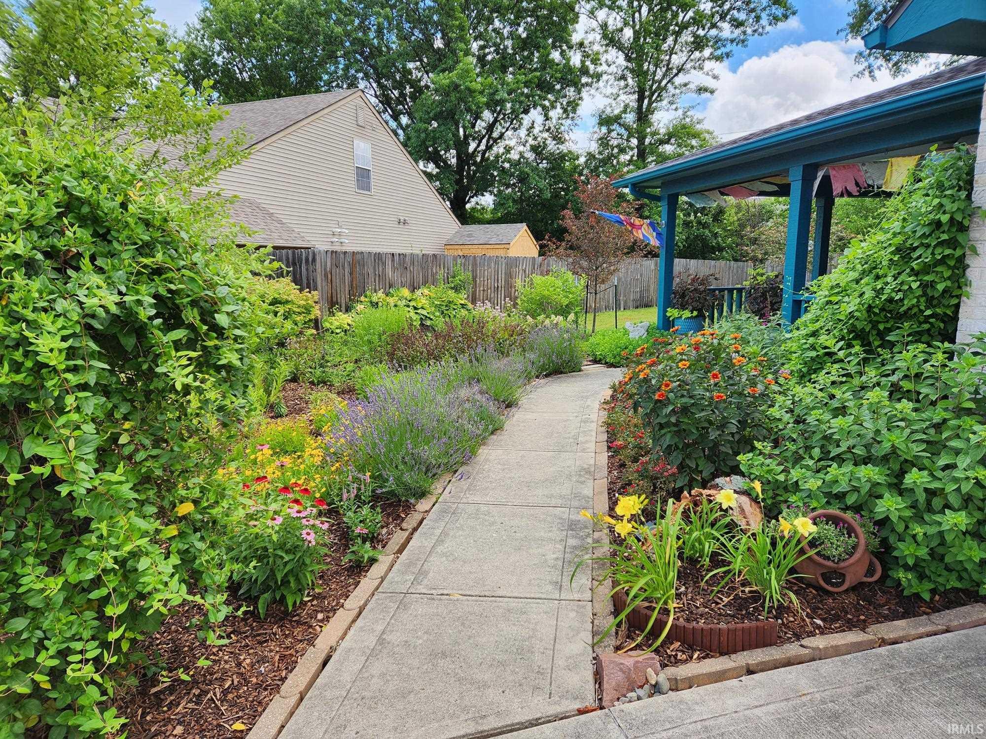 Concrete pathway bordered by lush garden beds featuring diverse plantings, including lavender and various flowering perennials