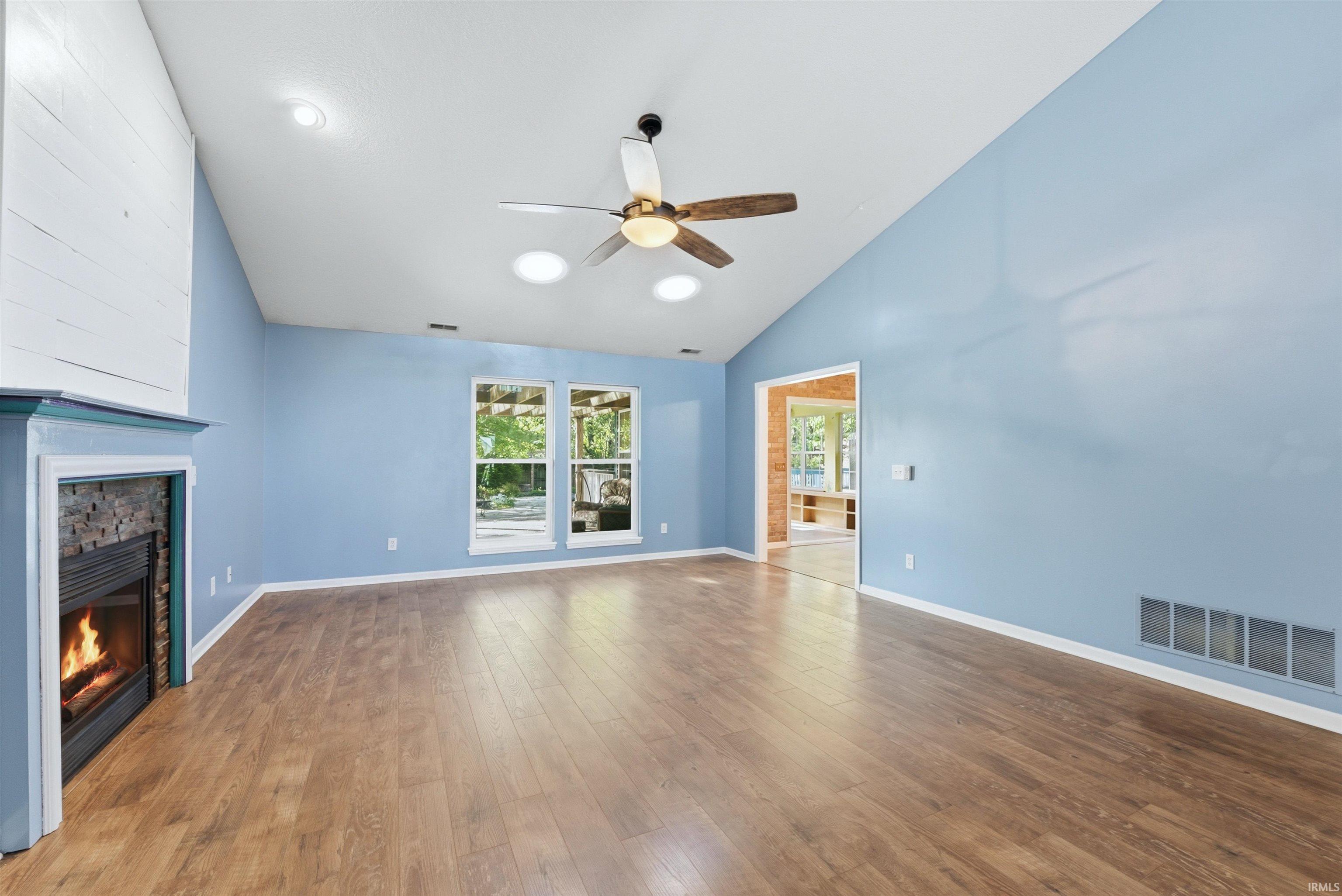 Spacious living area featuring wood-finish flooring, a stone-surround fireplace with a white shiplap-style facade, and a vaulted ceiling with a ceiling fan