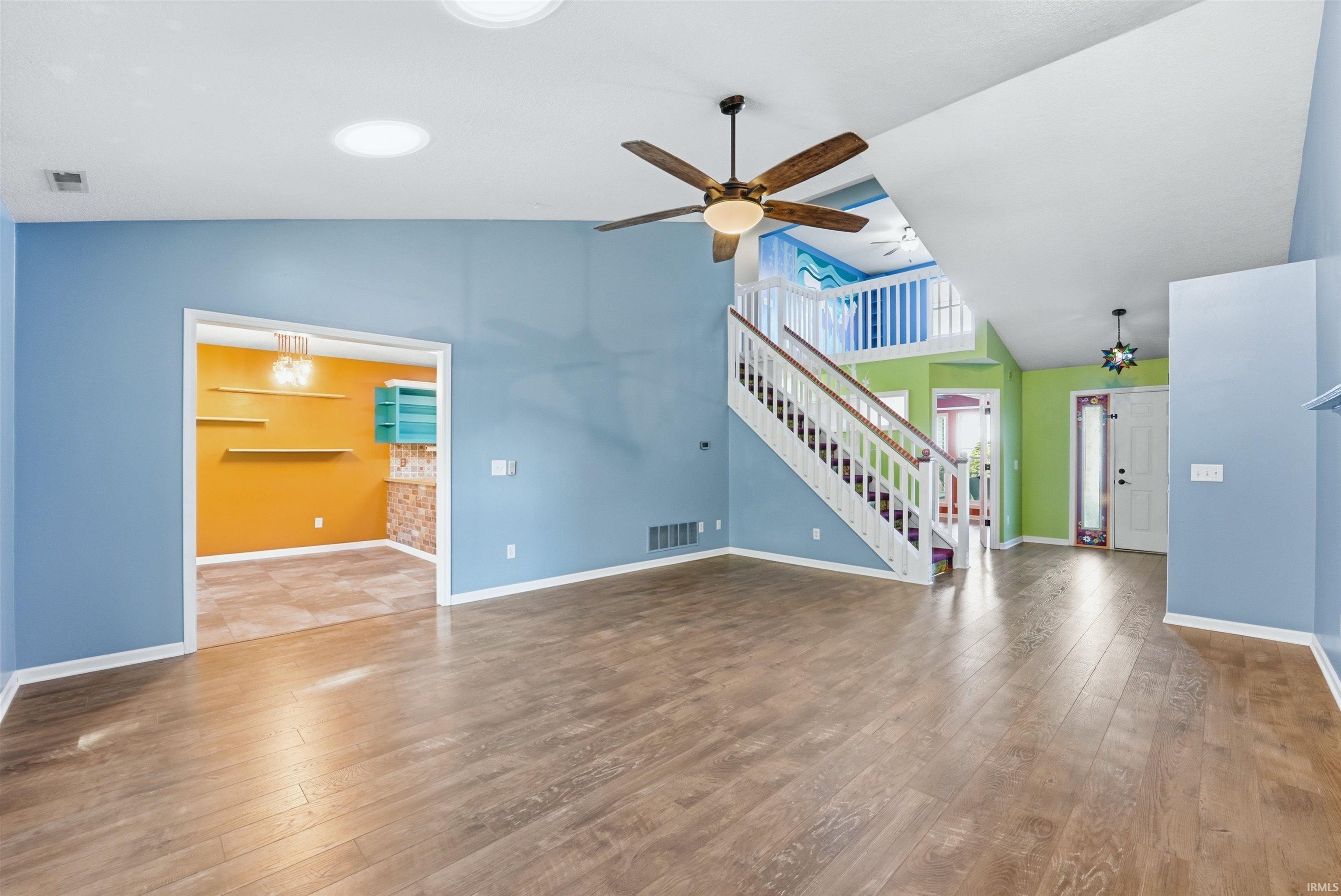 Spacious interior featuring wood-finish flooring, vaulted ceilings, and a prominent staircase with white railings
