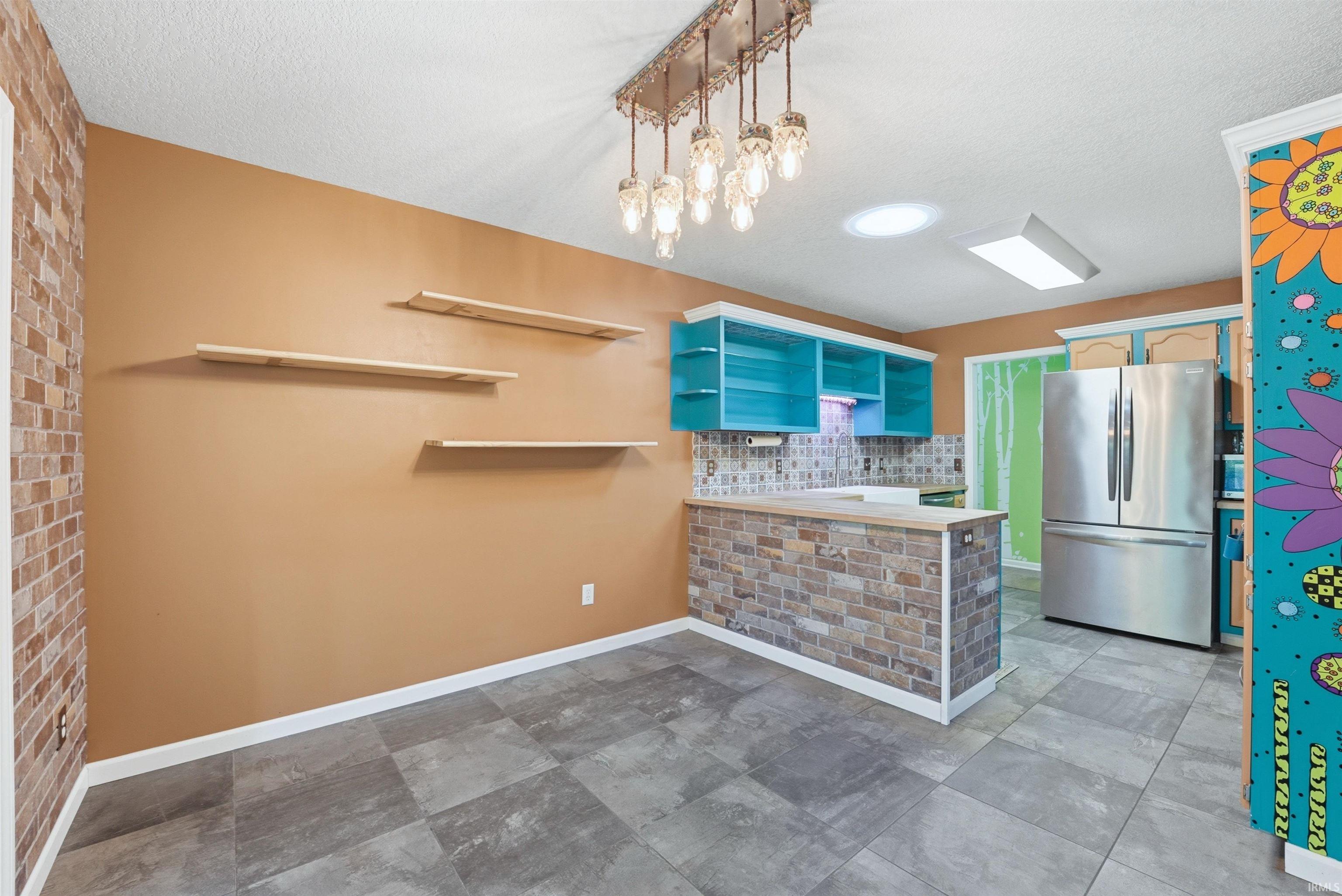 Open-concept kitchen and dining area featuring stone-look flooring, a brick-patterned bar, teal cabinetry, and a statement chandelier