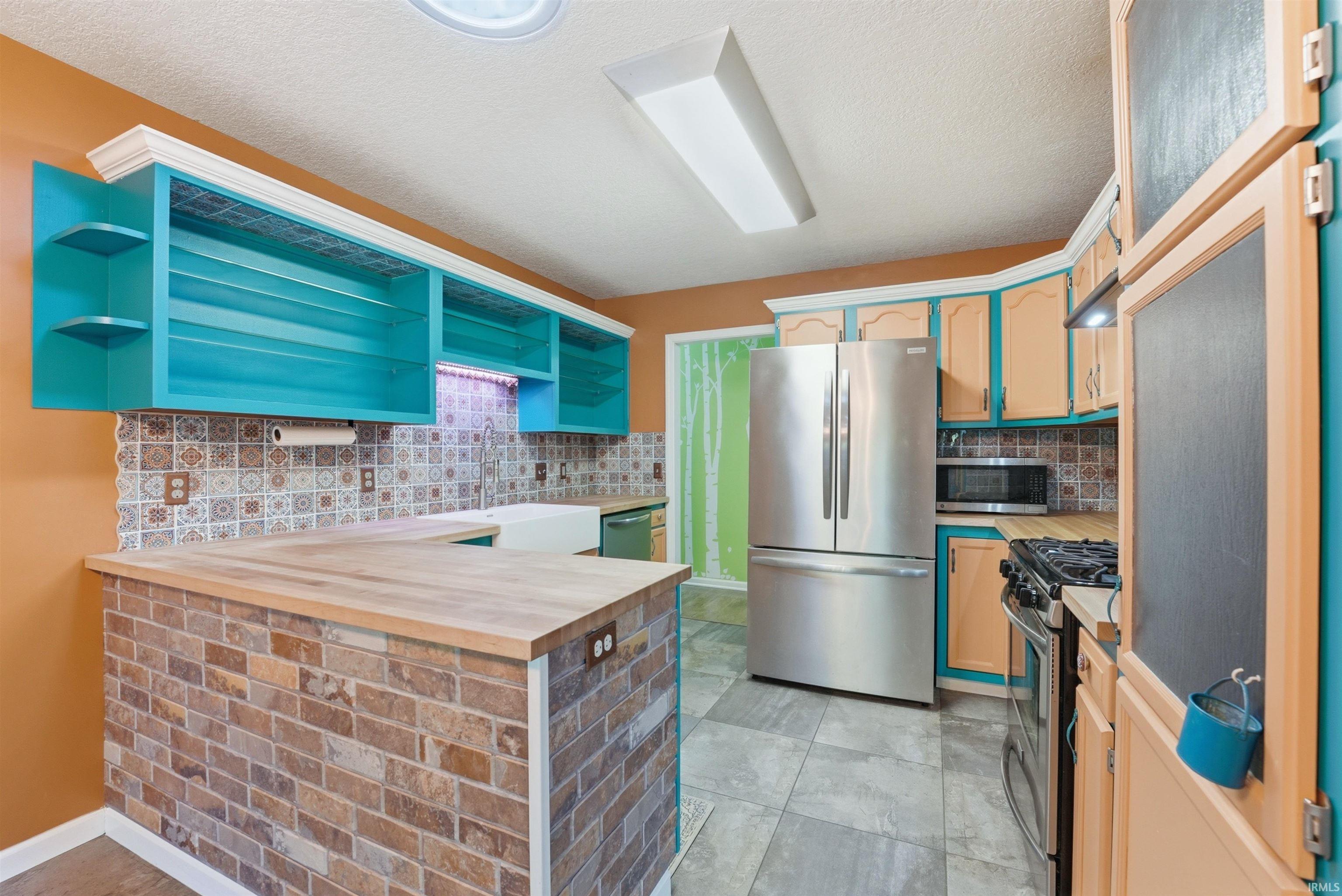 Kitchen featuring a brick accent island with a wood-finish countertop, patterned tile backsplash, and blue and beige cabinetry