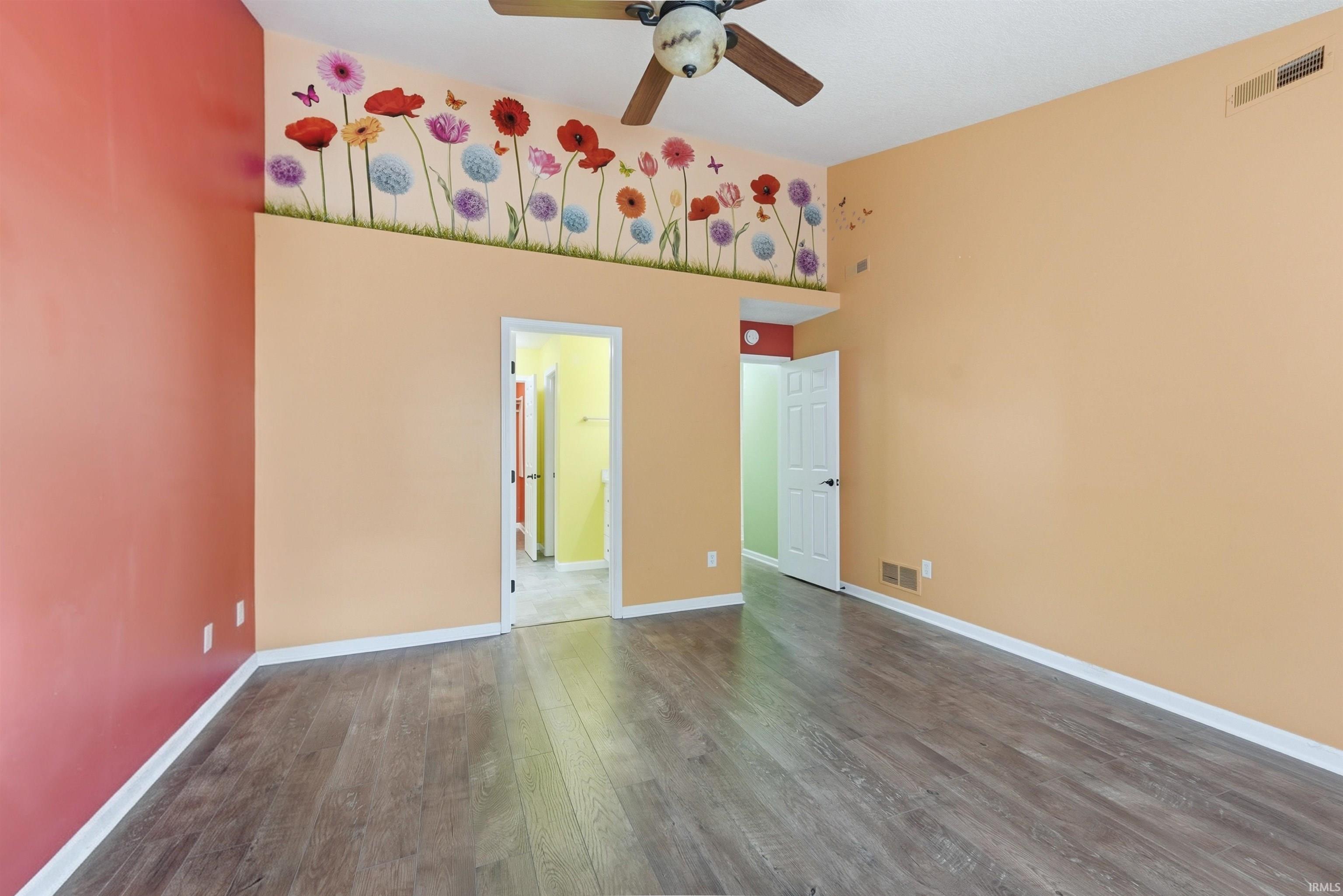 Spacious room featuring wood-finish flooring, a ceiling fan, and vibrant wall accents