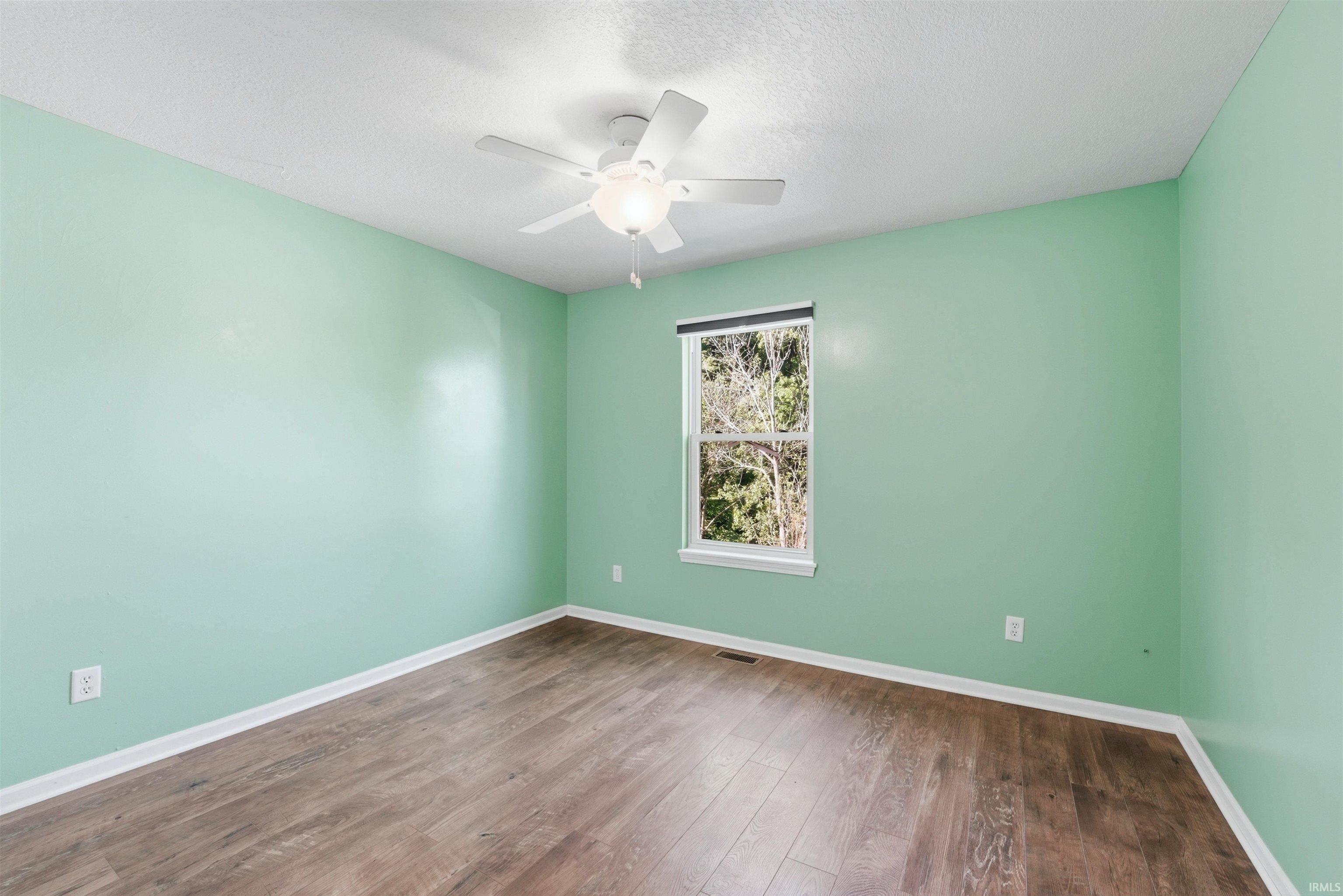 Room featuring wood-finish flooring, light green walls, a window with exterior views, white trim, and a ceiling fan with light fixture