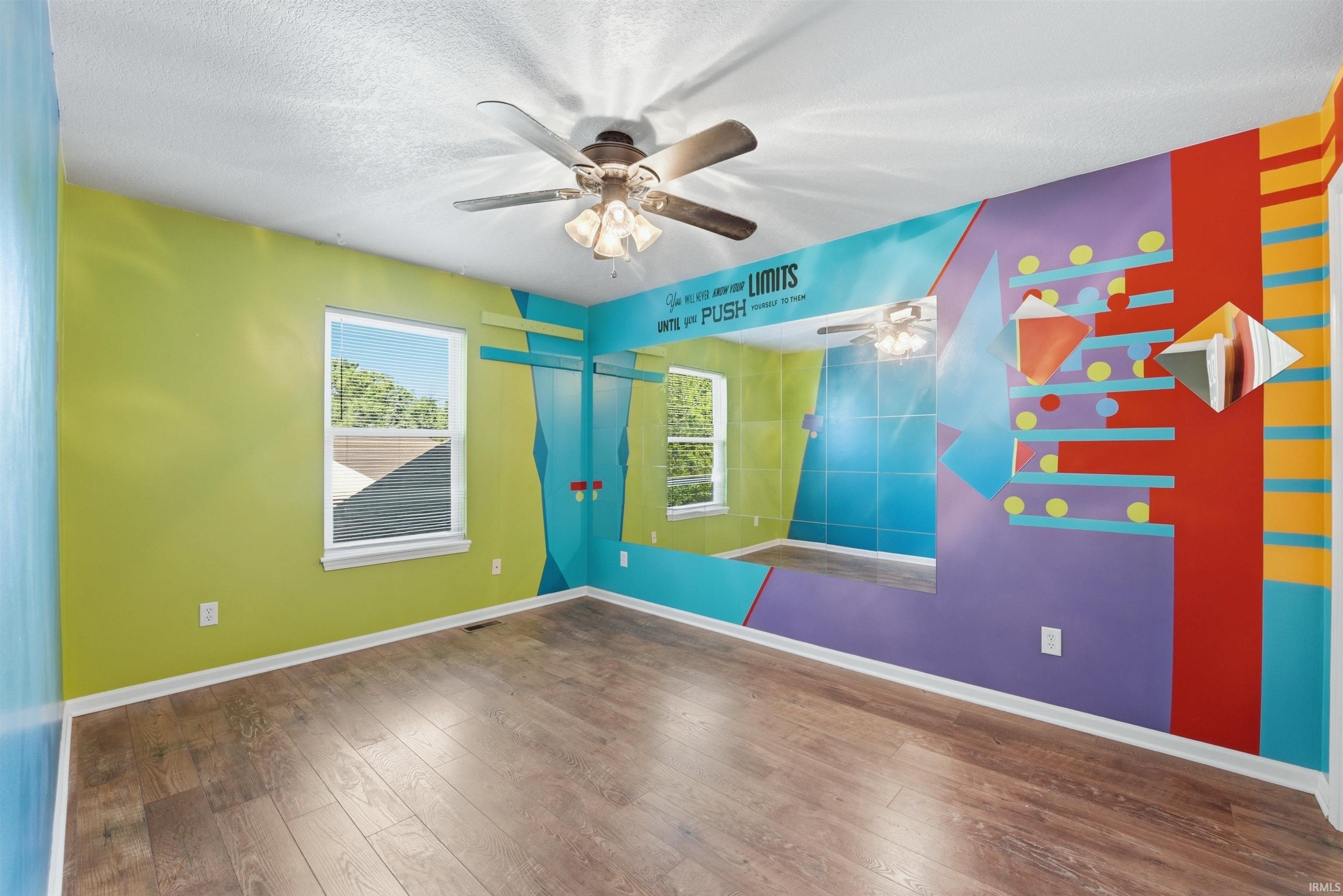 Vibrantly colored interior space featuring wood-finish flooring, white baseboards, and a ceiling fan with integrated lighting