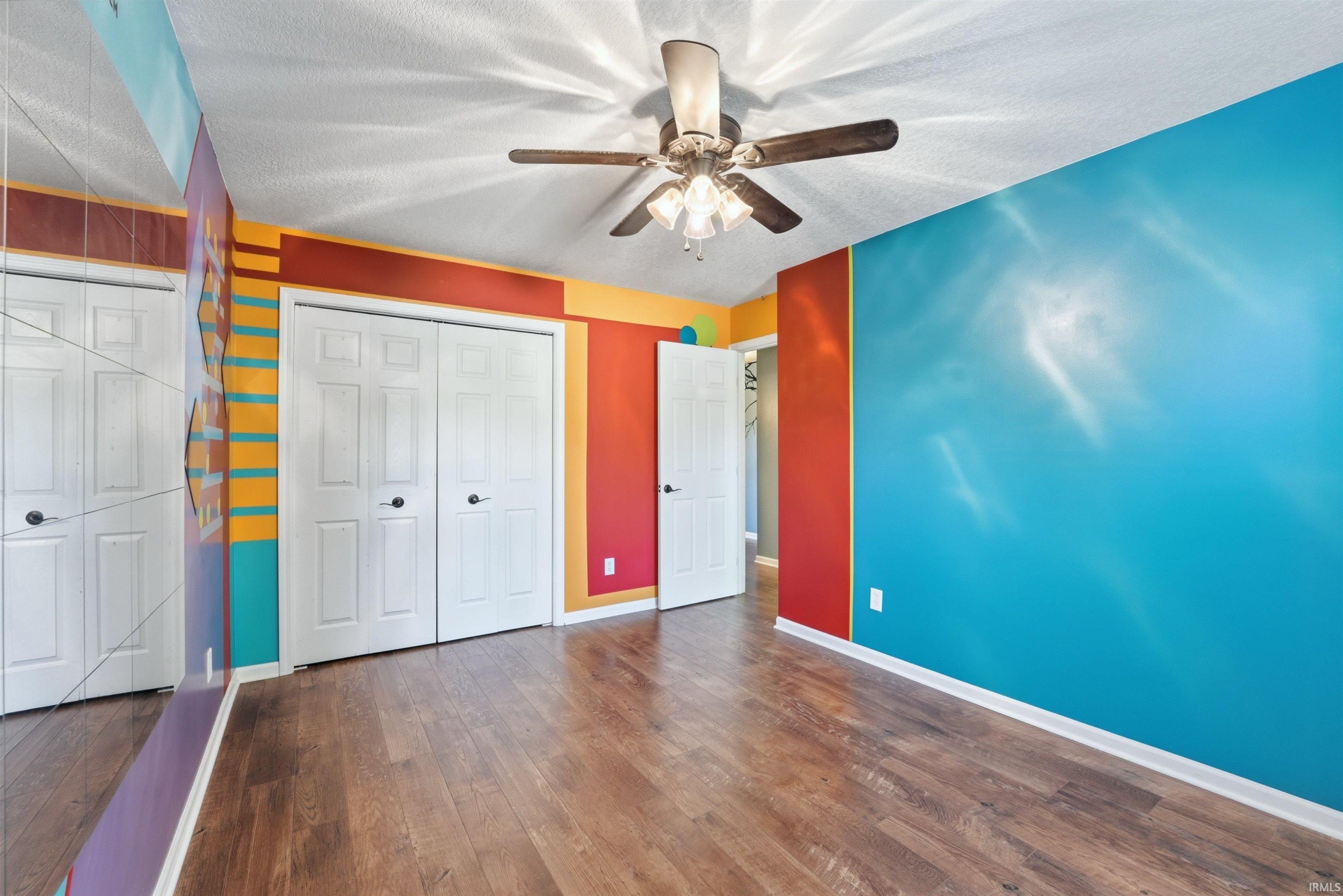 Expansive room featuring wood-finish flooring, a ceiling fan with integrated lighting, and white baseboards