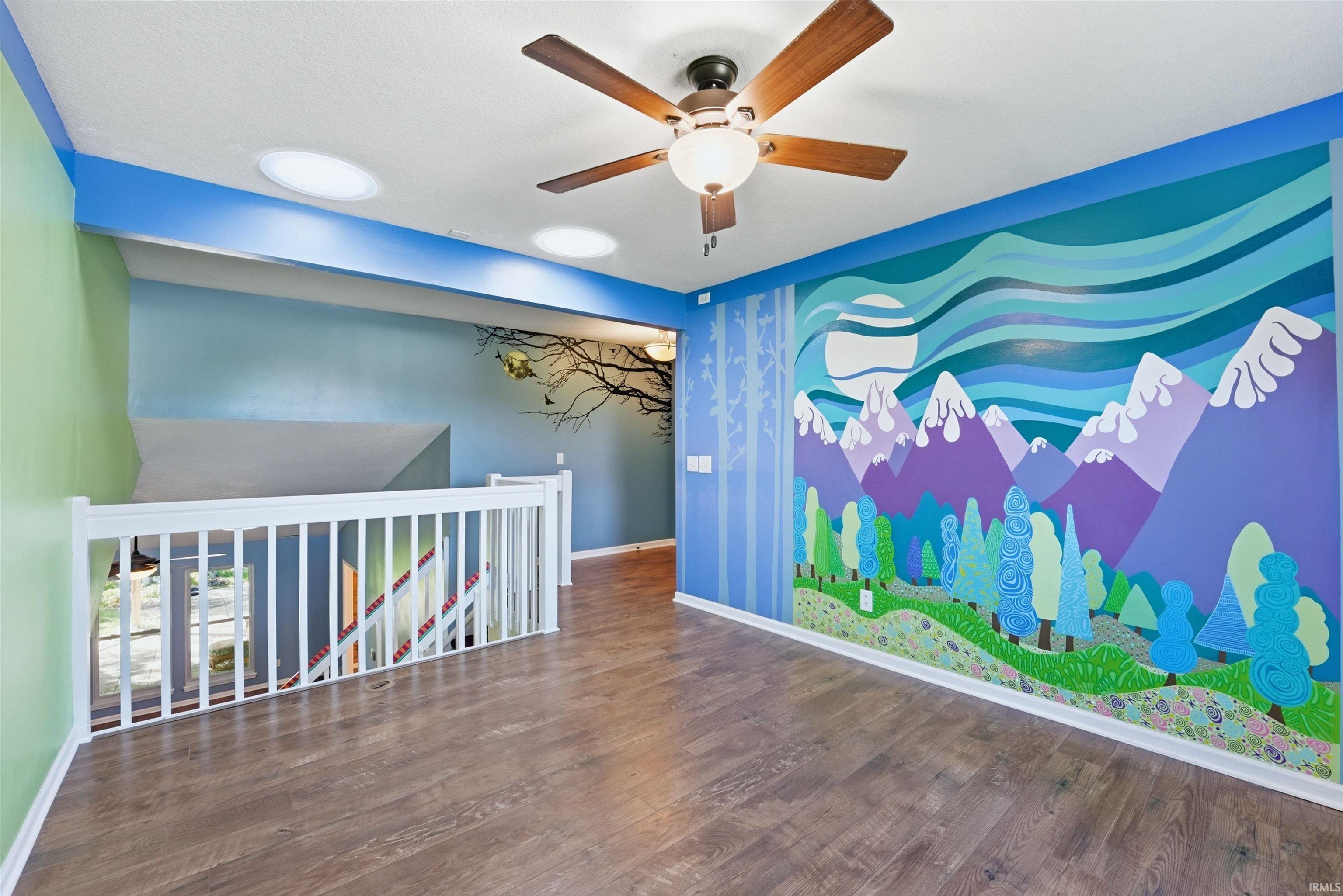 Spacious room featuring wood-finish flooring, a ceiling fan with light fixture, and two ceiling-mounted circular light fixtures