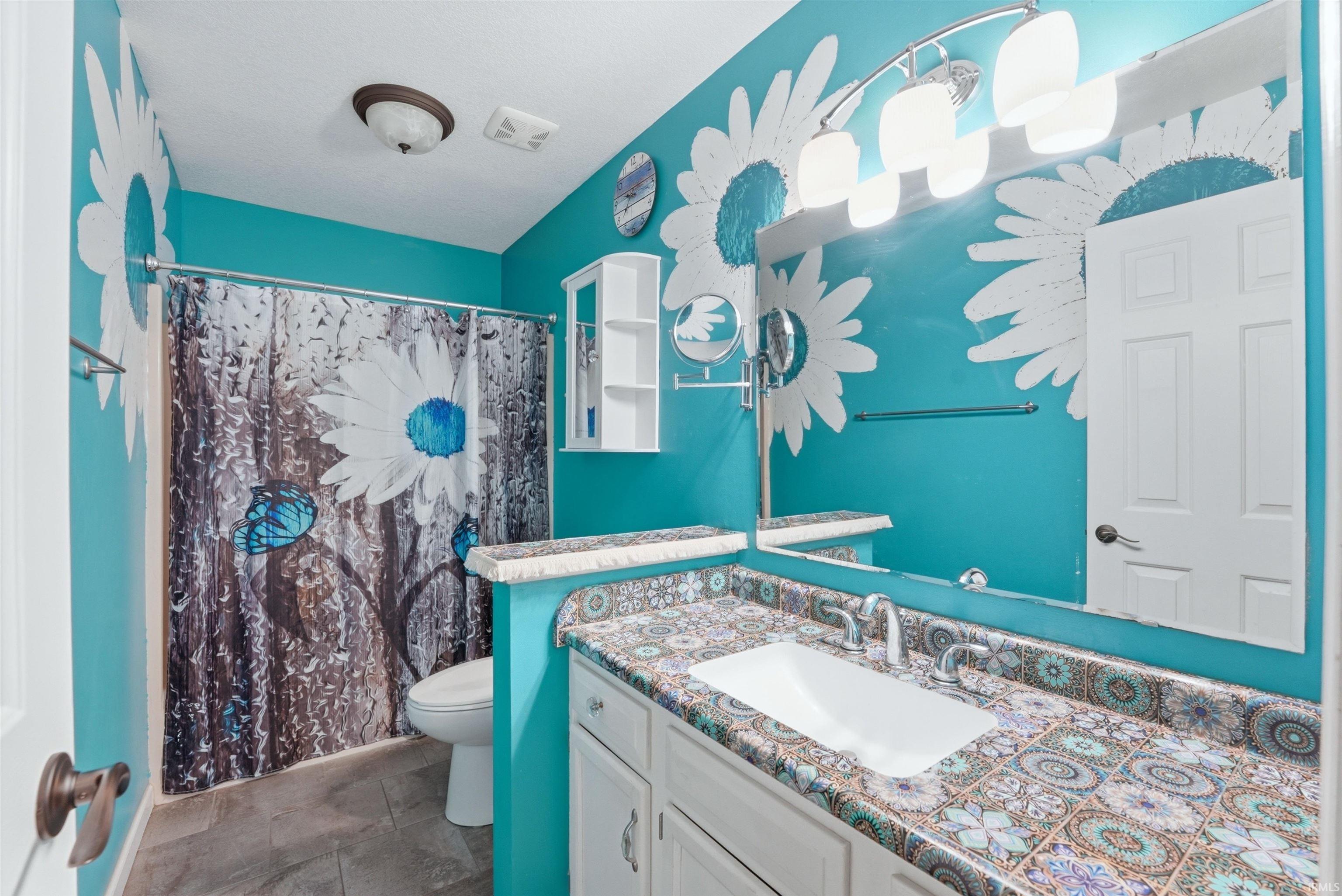 Bathroom featuring a single vanity with an integrated sink, mosaic-patterned countertop, and a large wall-mounted mirror