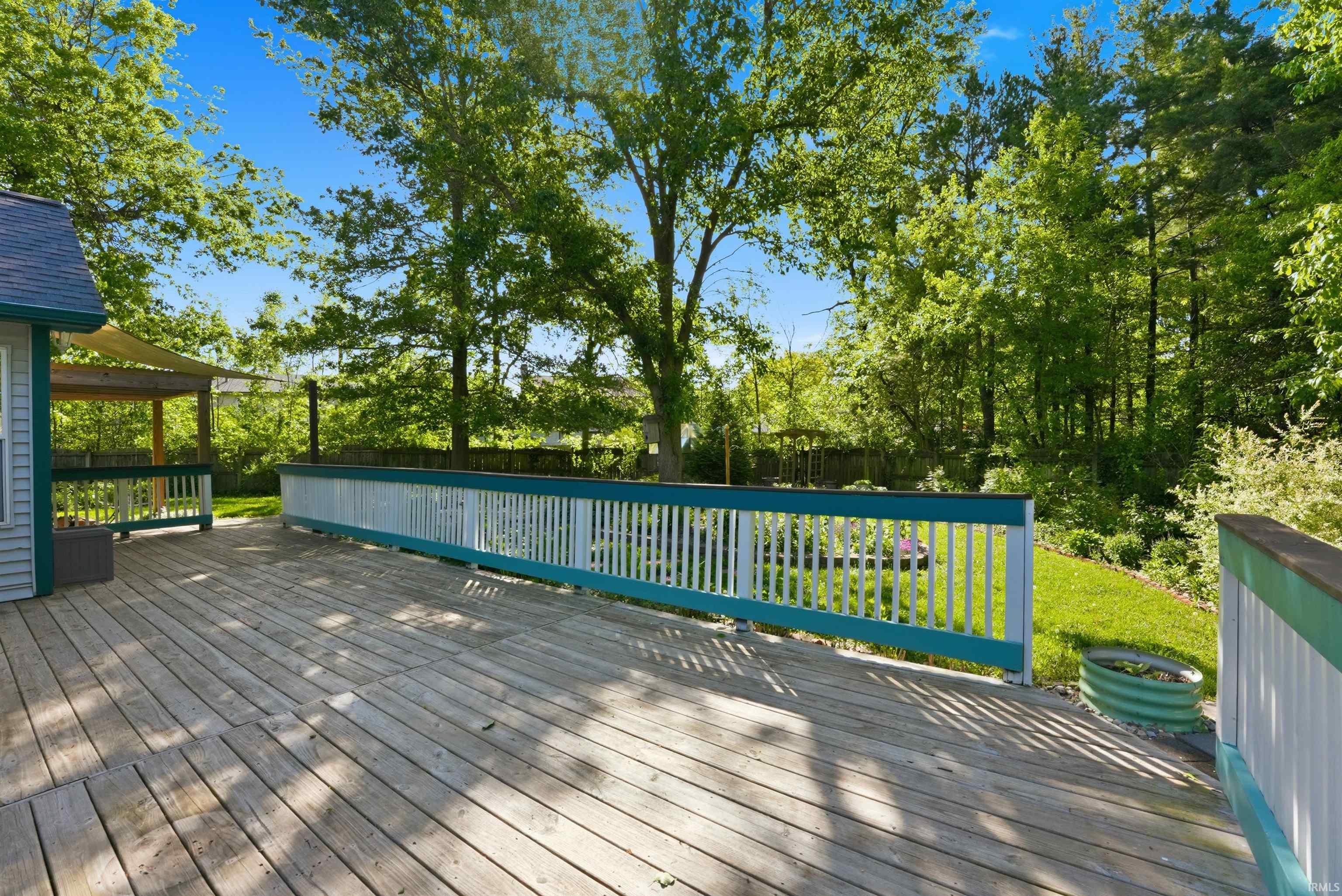 Expansive wood deck with white and teal railing, featuring a partial pergola structure