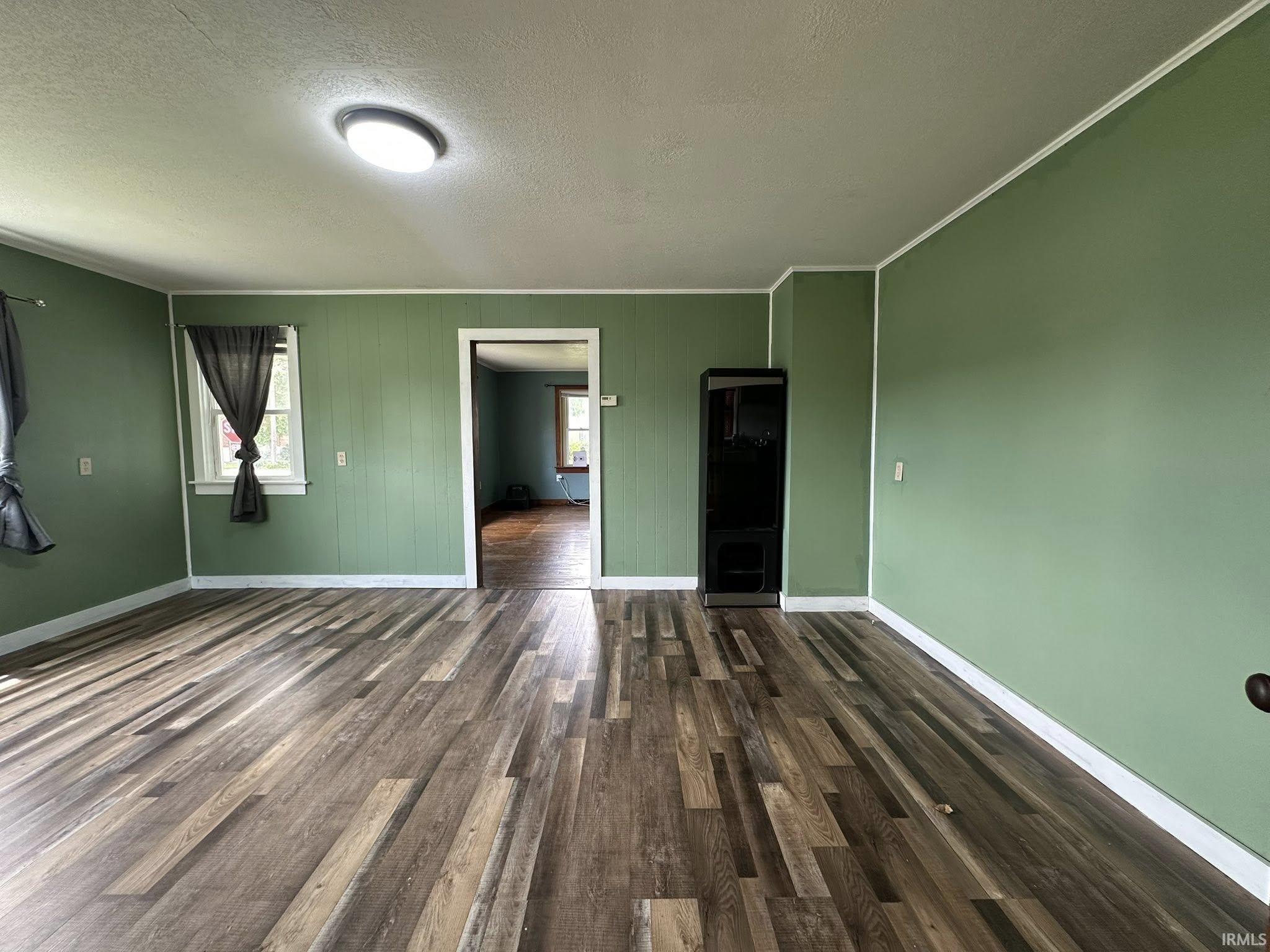 Spacious room featuring wood-finish flooring, light green walls, a flush-mount ceiling light, and white trim throughout