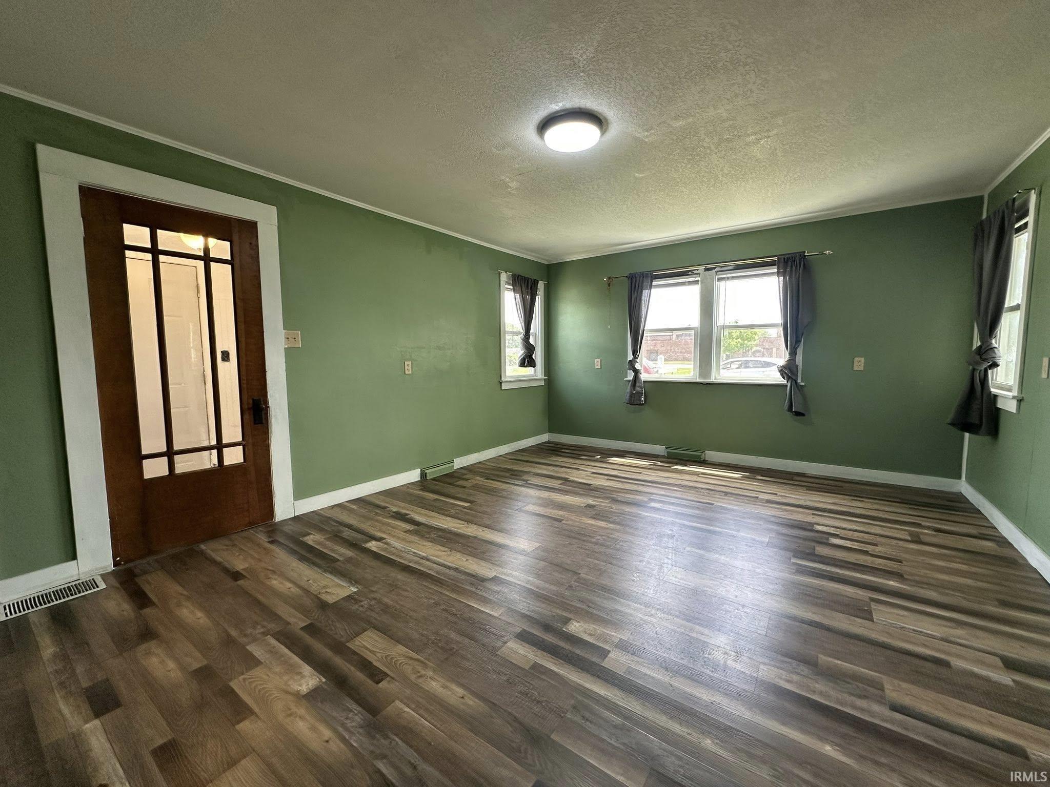 Spacious room featuring wood-finish flooring, multiple windows, a ceiling-mounted light fixture, and a paneled door with glass inserts