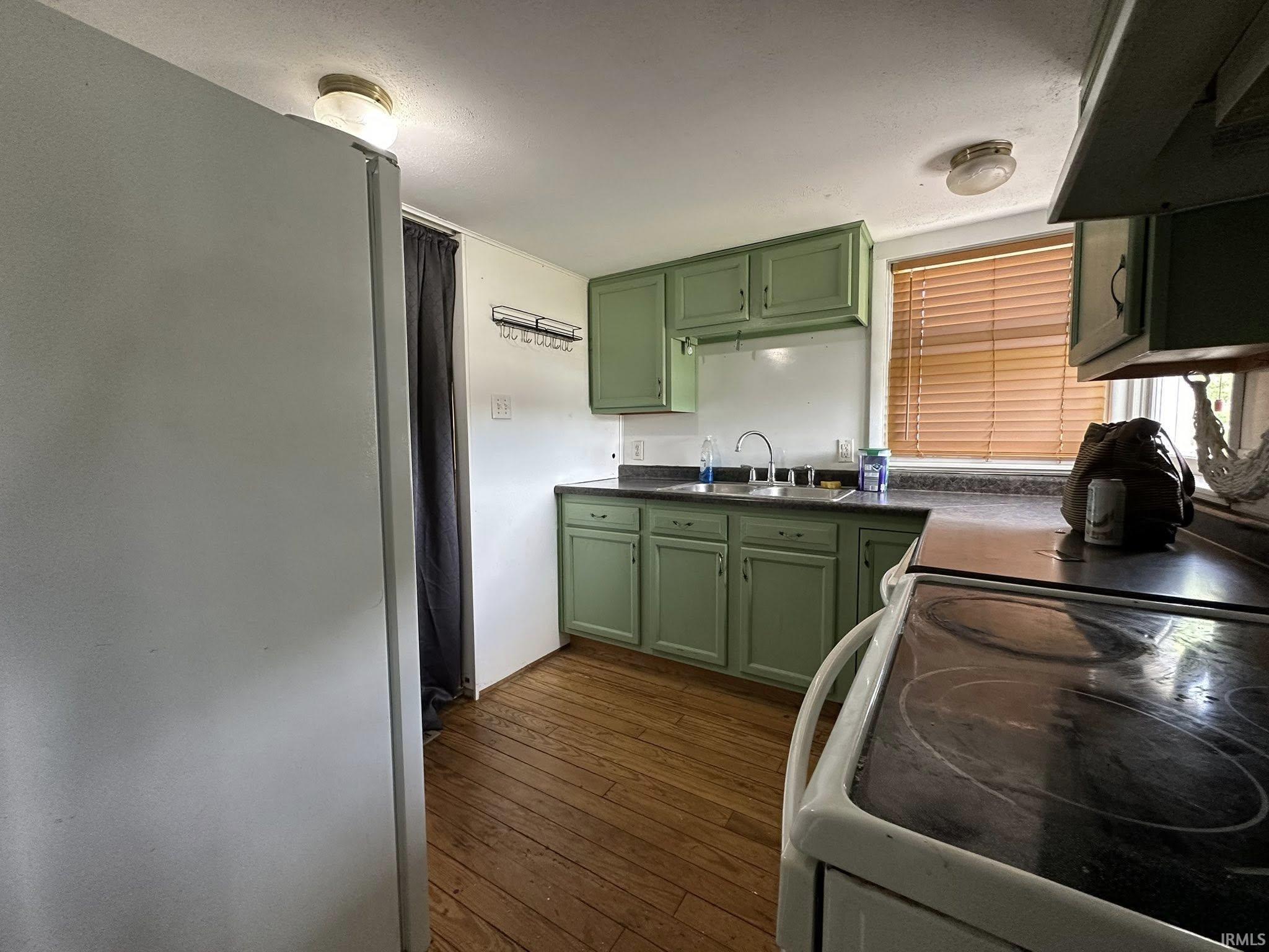 Kitchen featuring wood-finish flooring, green cabinetry, a window with blinds, and a built-in double basin sink