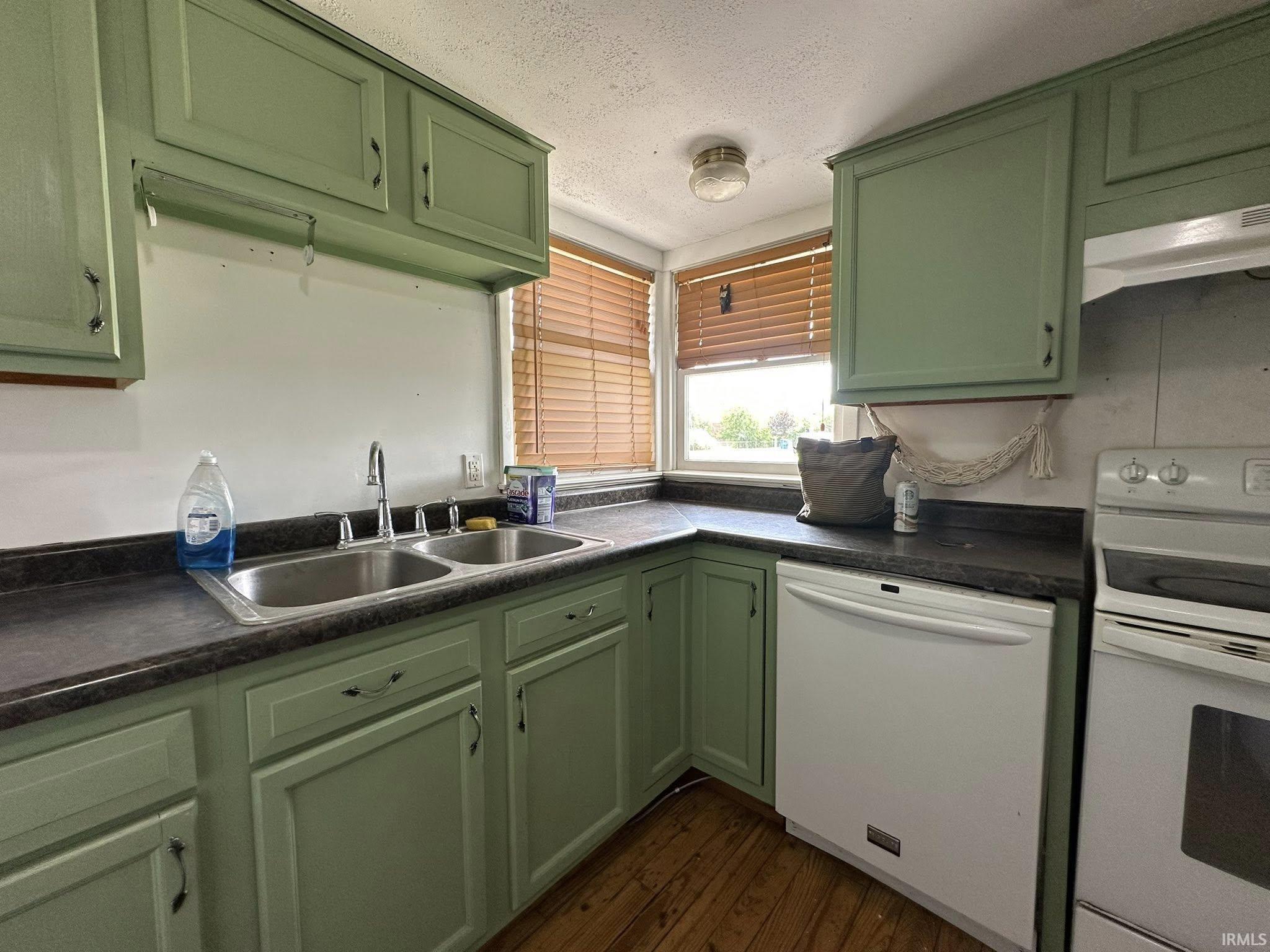Kitchen featuring green cabinetry, dark countertops, a double basin stainless steel sink, and wood-finish flooring