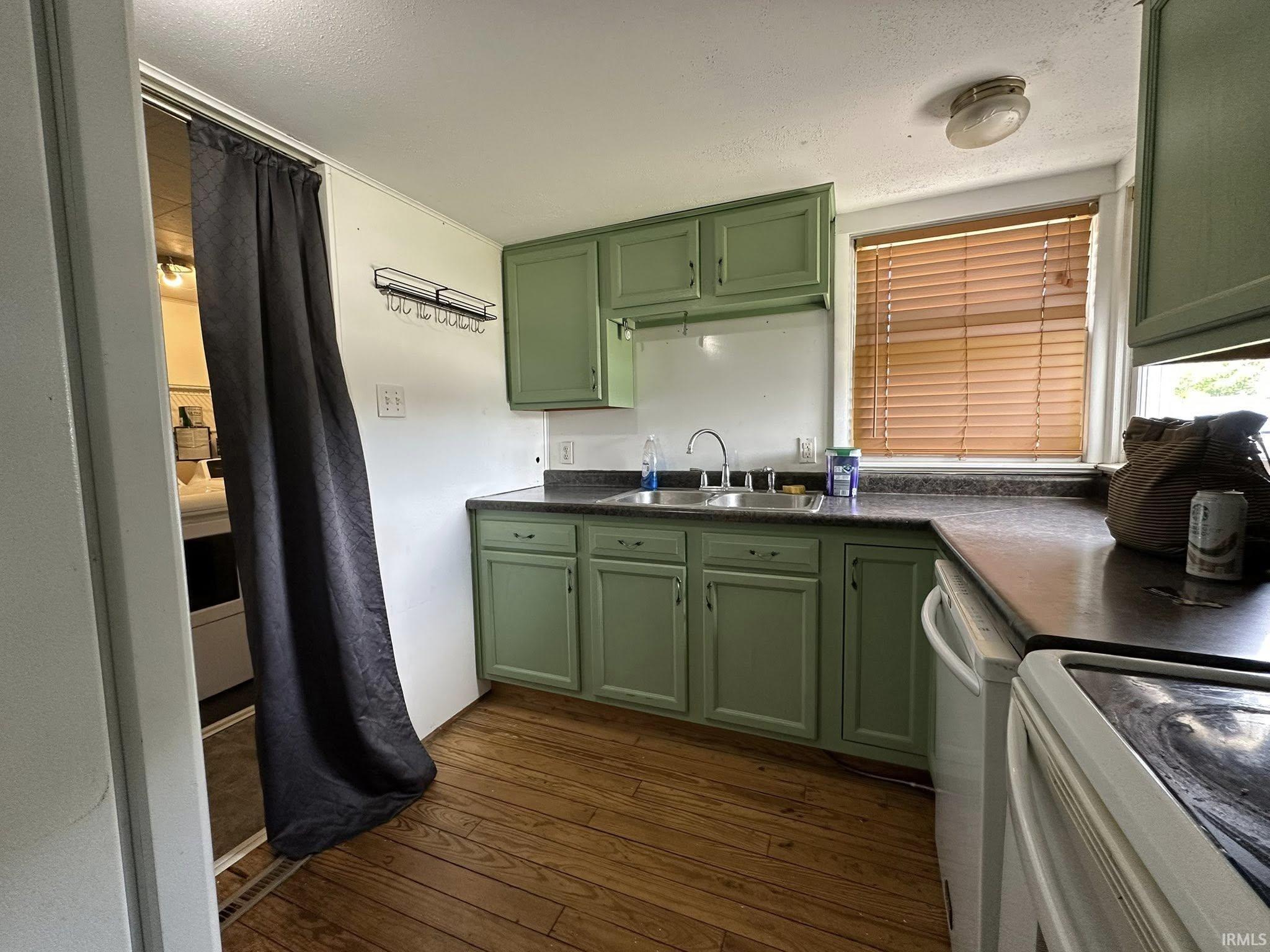 Kitchen featuring wood-finish flooring, green cabinetry, a dual basin stainless steel sink, and a window with horizontal blinds
