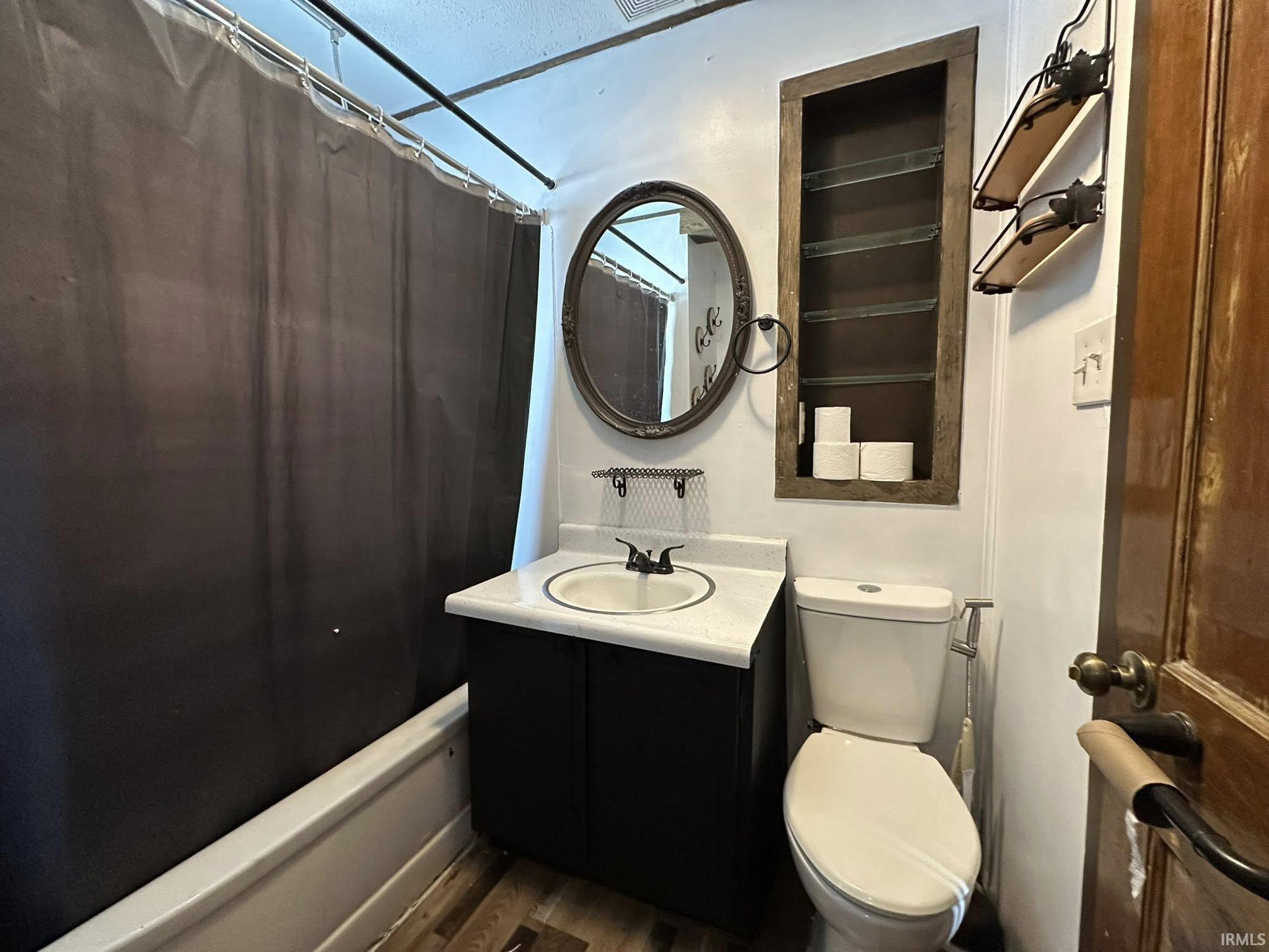 Bathroom featuring a white bathtub, a dark vanity with a white countertop and integrated sink, an oval wall mirror, and an inset wall shelf