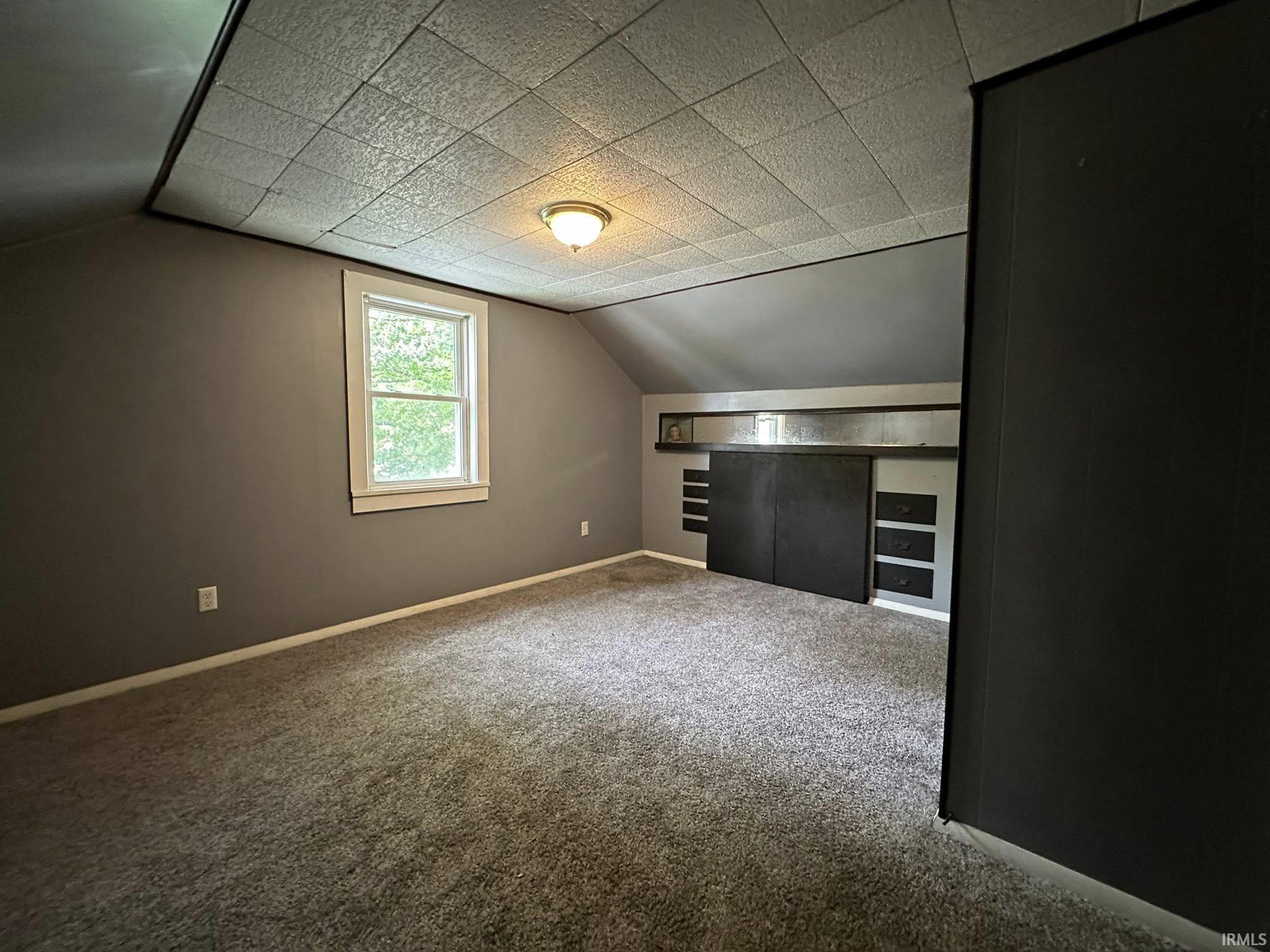 Carpeted room with a window, sloped ceilings, and a flush-mount light fixture