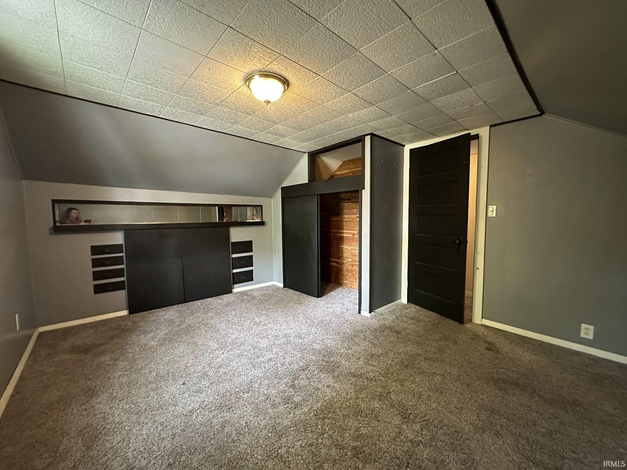 Carpeted interior space featuring a textured acoustic tile ceiling with an overhead light fixture