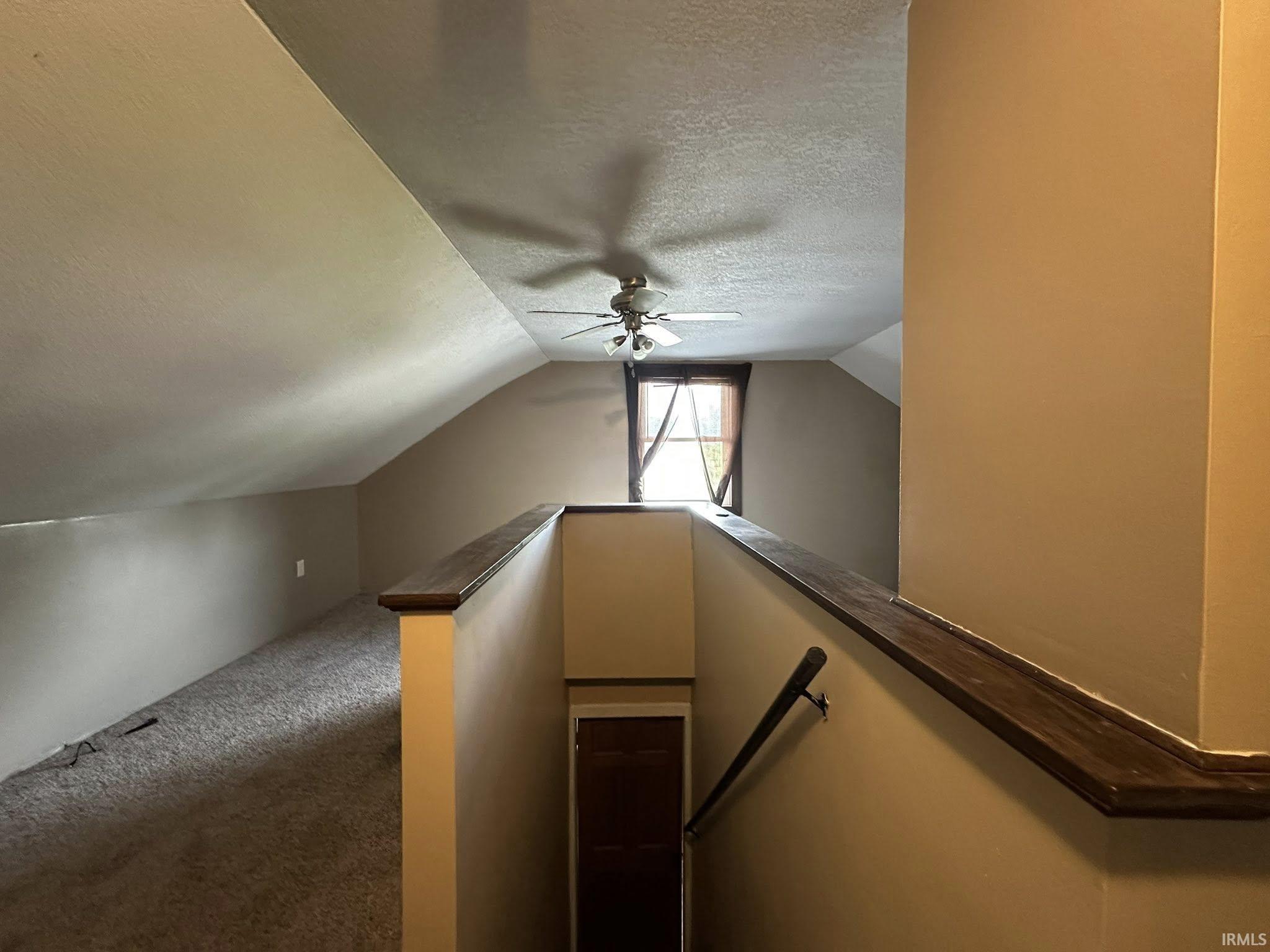 Carpeted loft area featuring a sloped ceiling, ceiling fan, and a single window