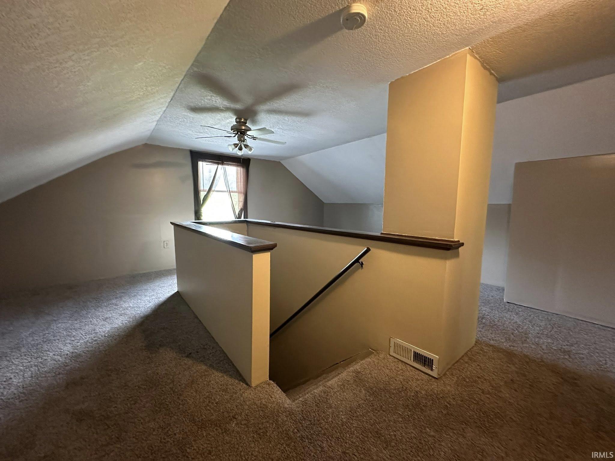 Carpeted loft area featuring a ceiling fan, sloped ceilings, and a window with natural light