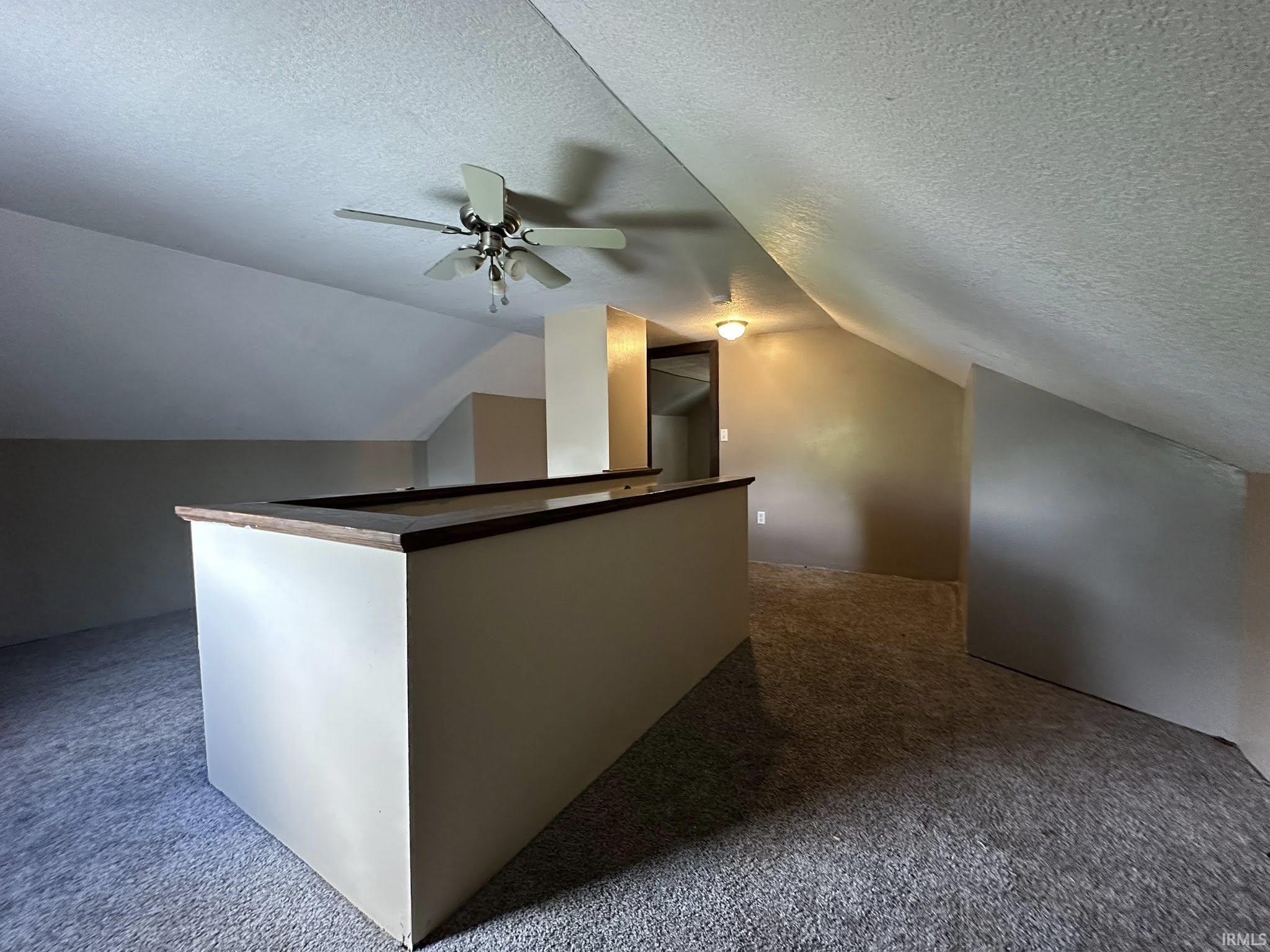 Expansive open space featuring sloped ceilings with a ceiling fan, neutral wall tones, and textured carpeting