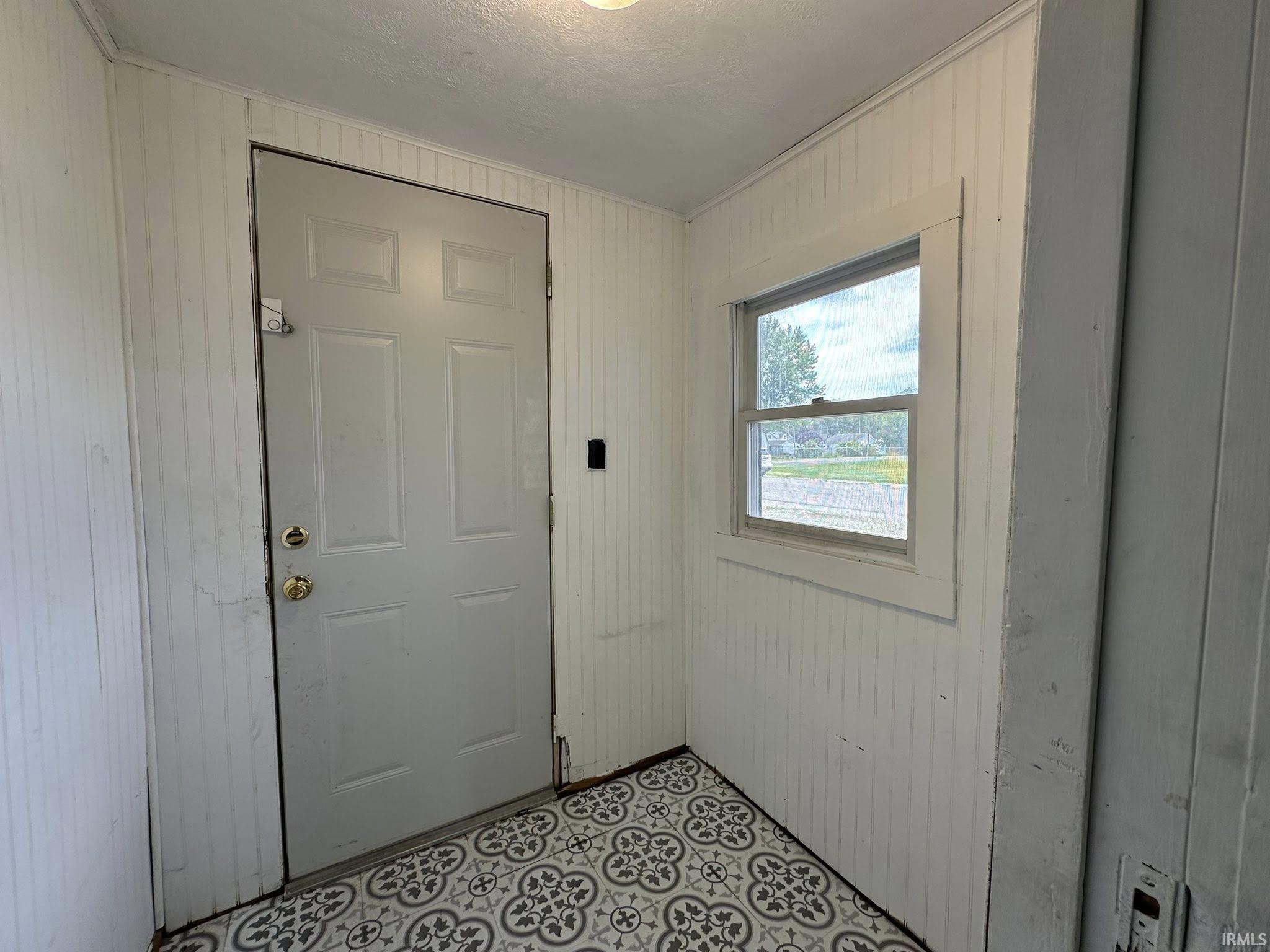 Entryway featuring patterned floor tiles, white paneled walls, a single window, and a light-colored door with brass-finish hardware