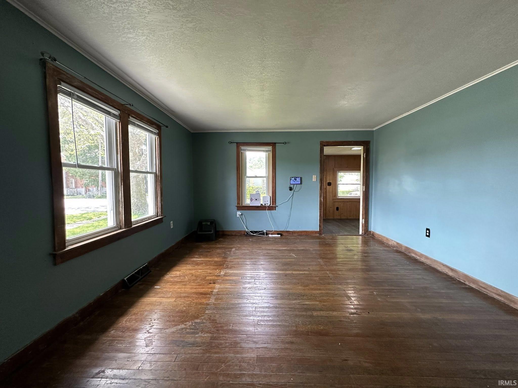 Spacious interior with wood-finish flooring, two large windows, and a doorway opening to an additional room