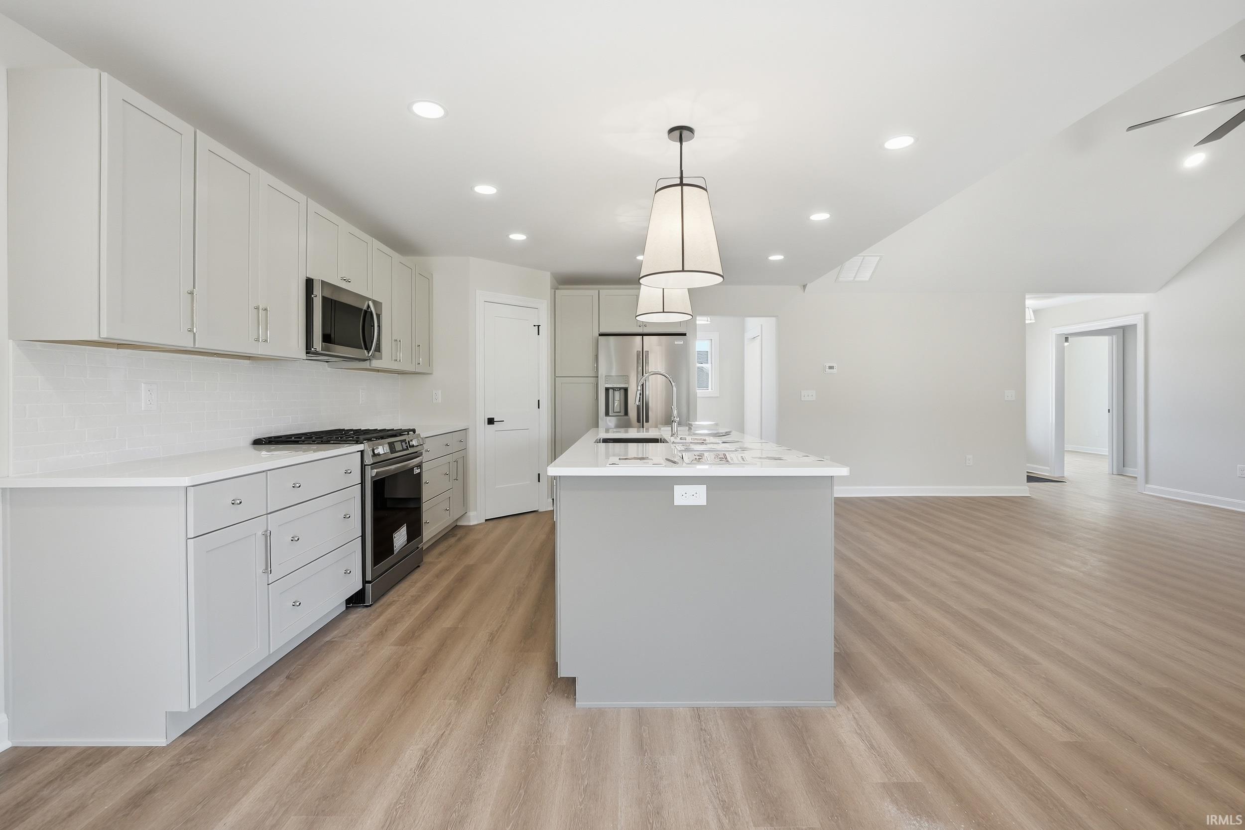 Modern kitchen featuring light-toned cabinetry, stainless steel appliances, and wood-finish flooring