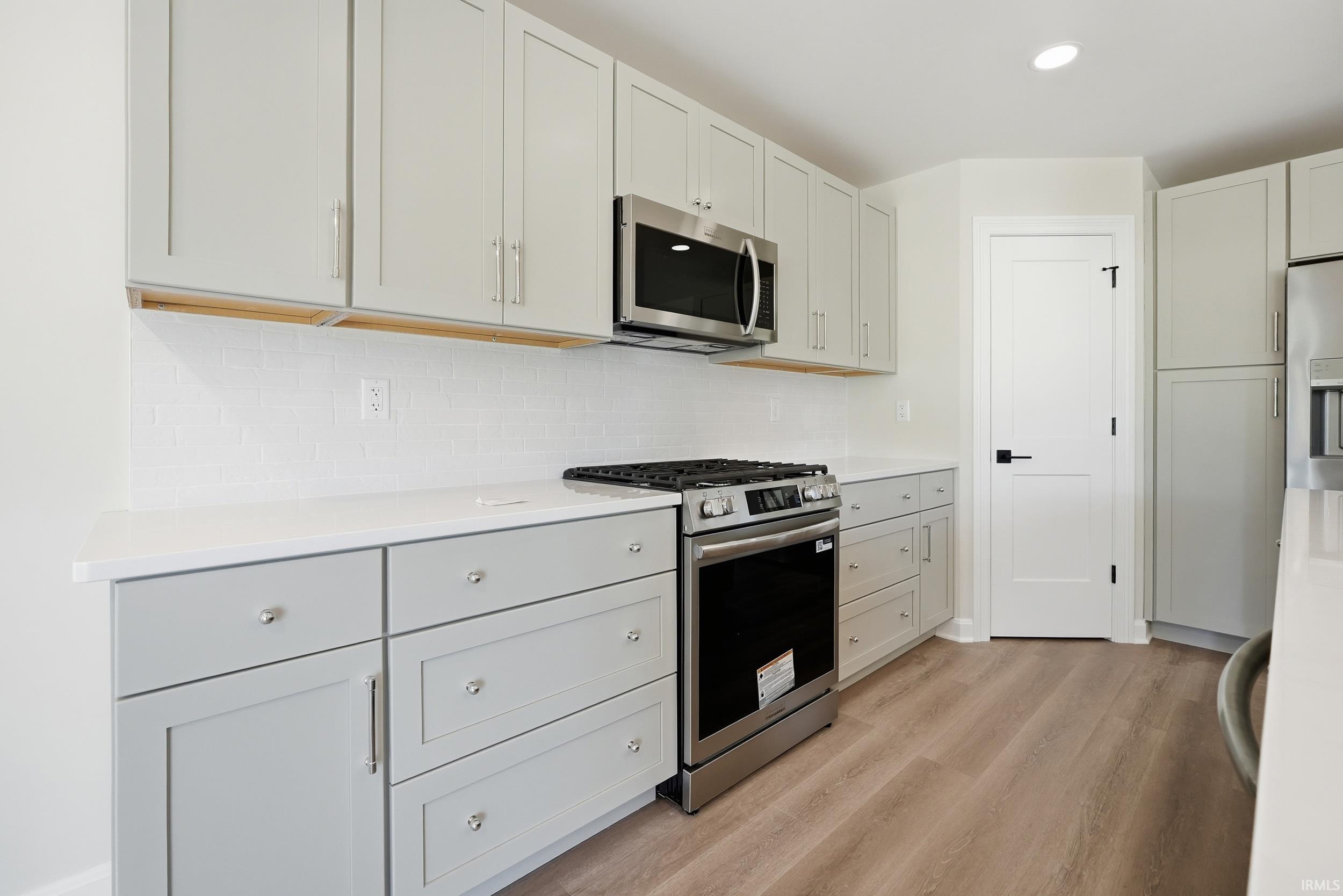 Modern kitchen featuring light-toned cabinetry, white countertops, stainless steel appliances, and wood-finish flooring