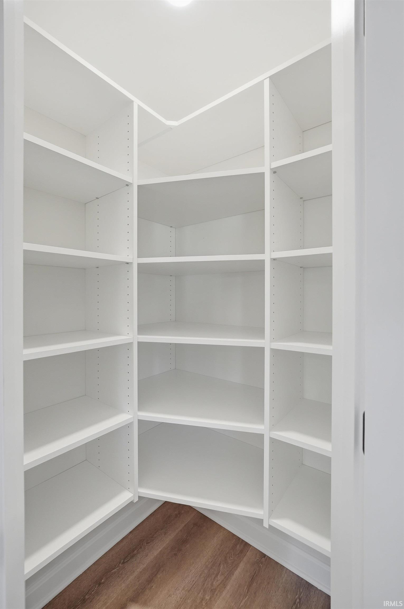 Walk-in pantry with extensive white shelving, wood-finish flooring, and recessed ceiling lighting
